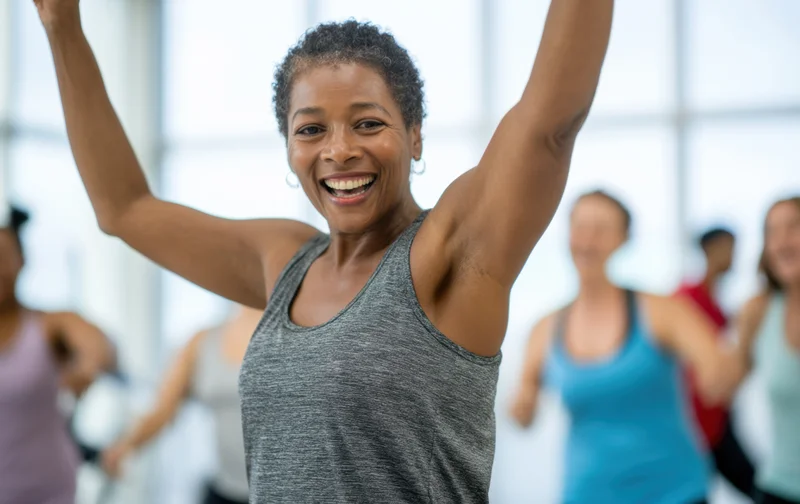 Smiling middle-aged african american woman leading a group fitness class with arms raised in a bright gym