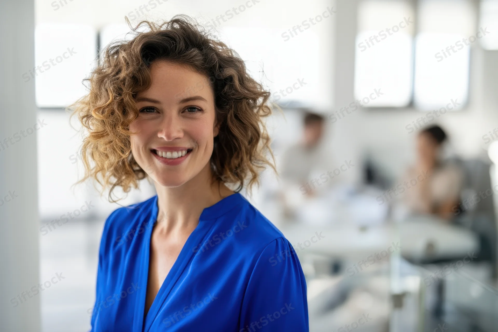 Smiling woman with curly hair in blue blouse standing in modern office space