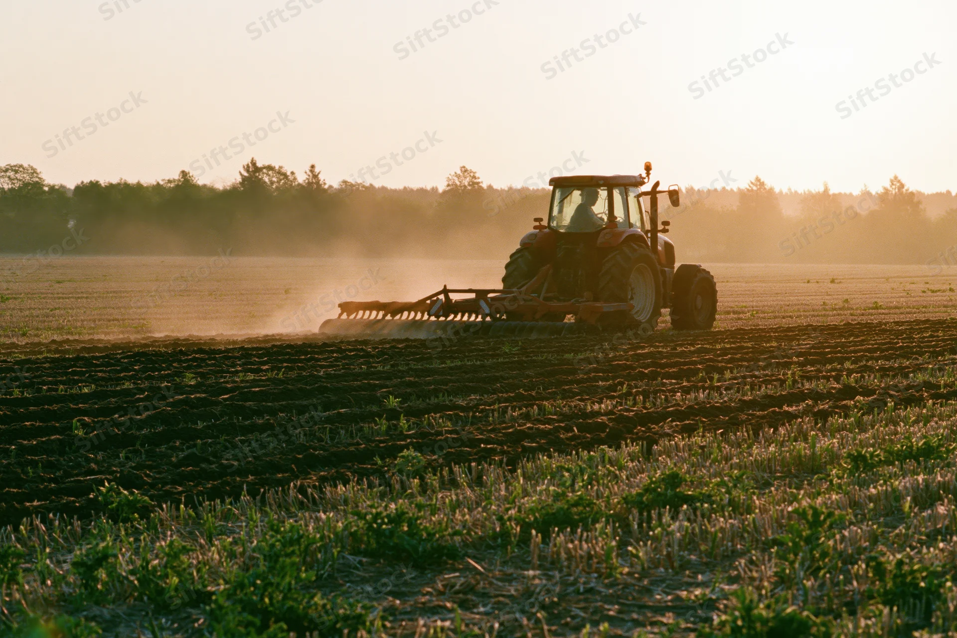 Farm tractor pulling a disc harrow across a flat agriculture