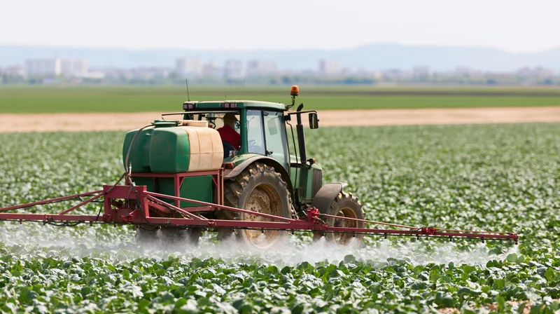 Green tractor with red boom sprayer applying pesticide in a crop field