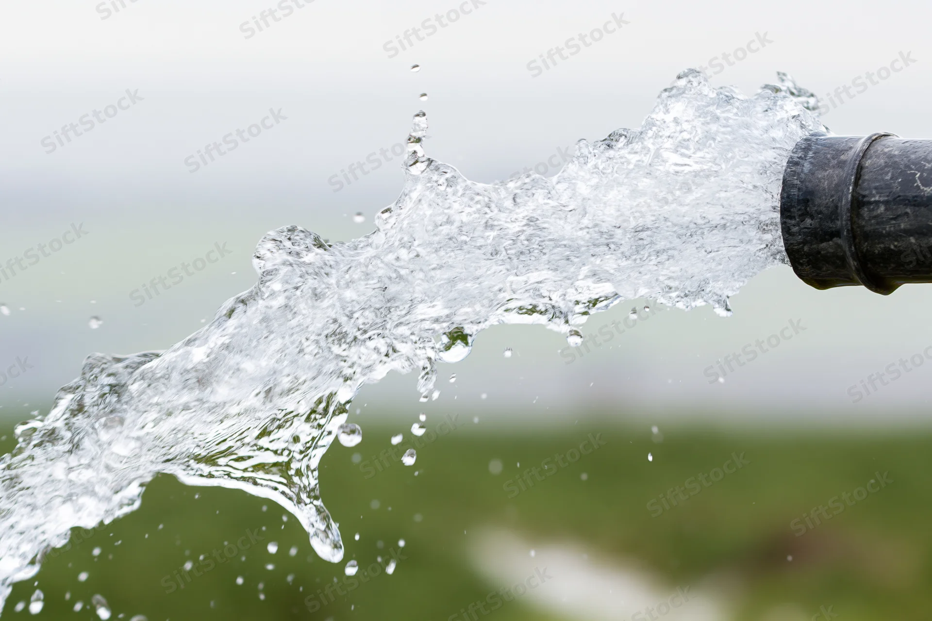 Forceful stream of clear water bursting from a garden hose in an outdoor setting