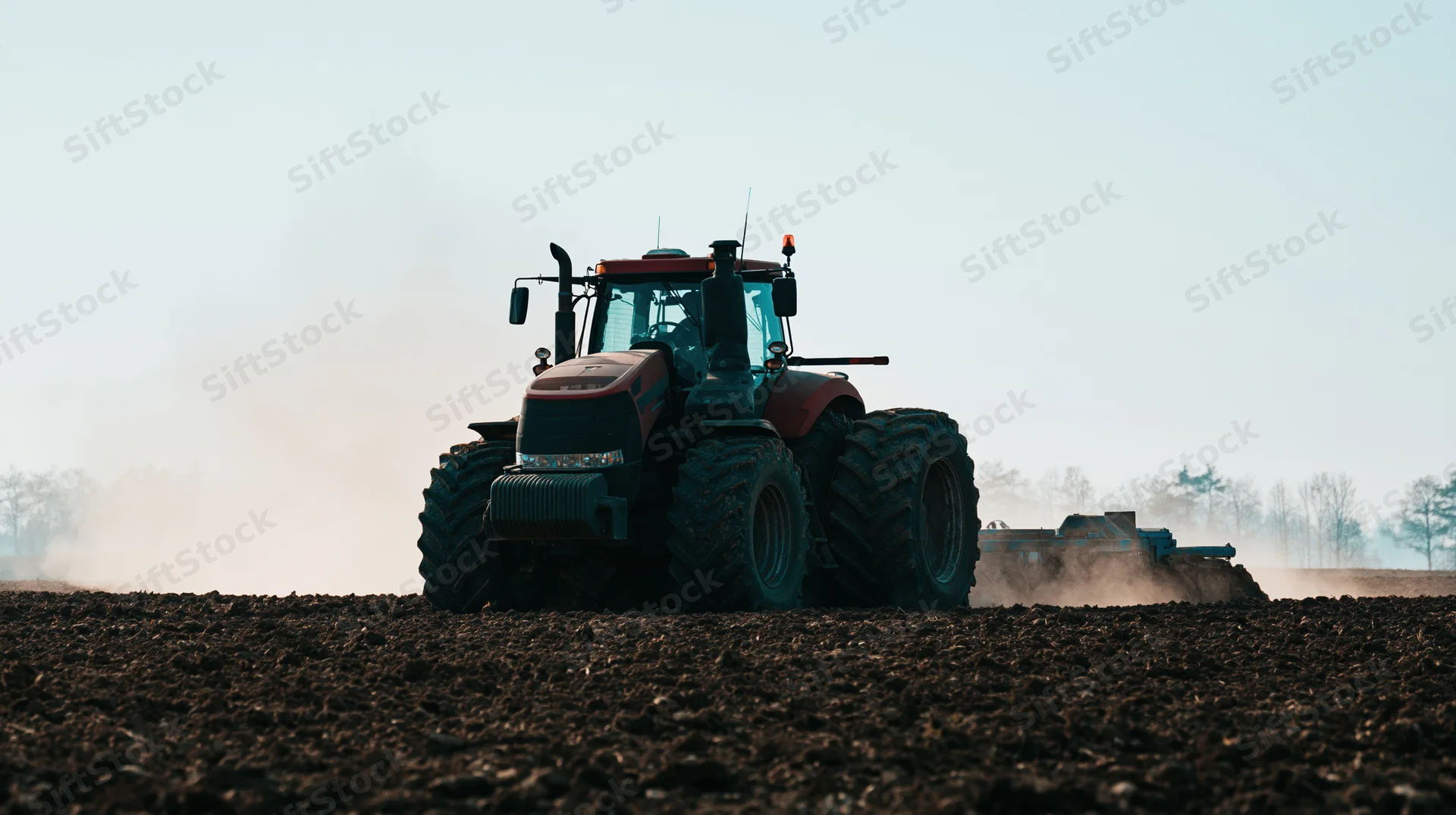 Large red tractor pulling tillage equipment across dark tilled field