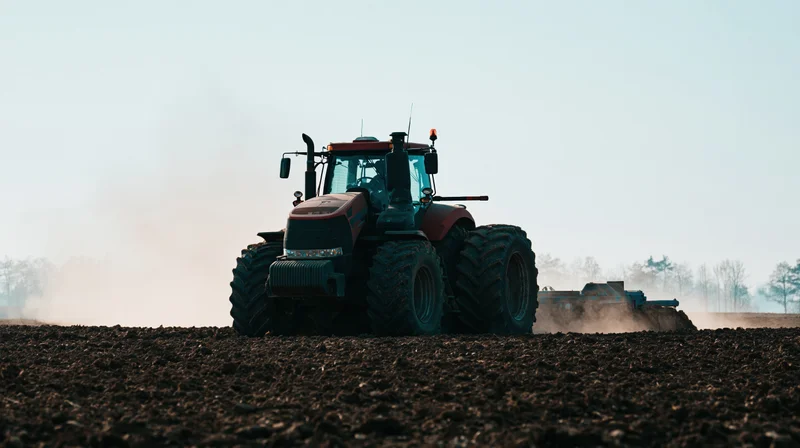 Large red tractor pulling tillage equipment across dark tilled field