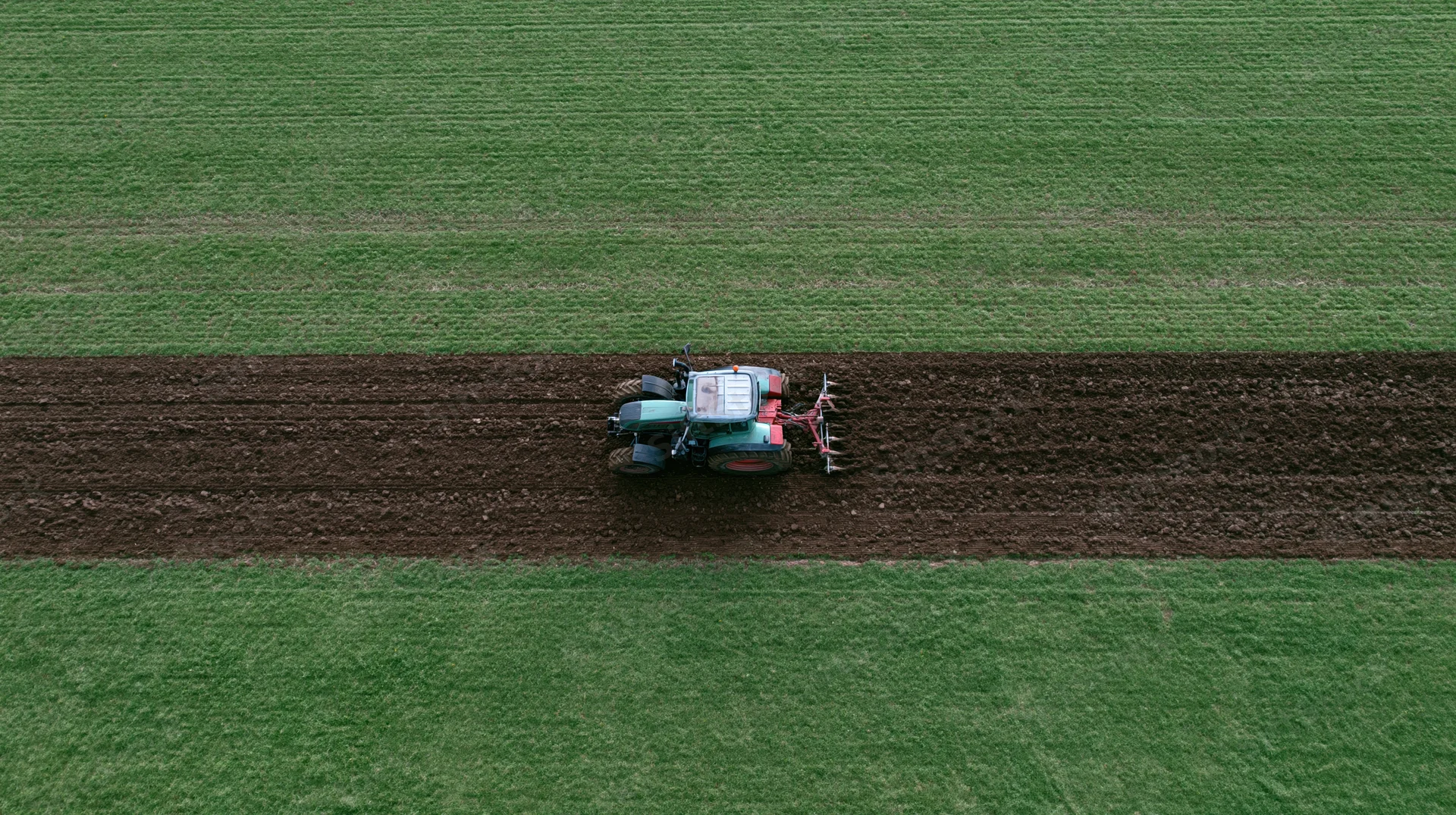 Tractor plowing a strip in a green field from above