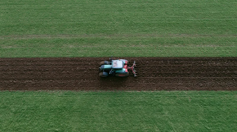 Tractor plowing a strip in a green field from above