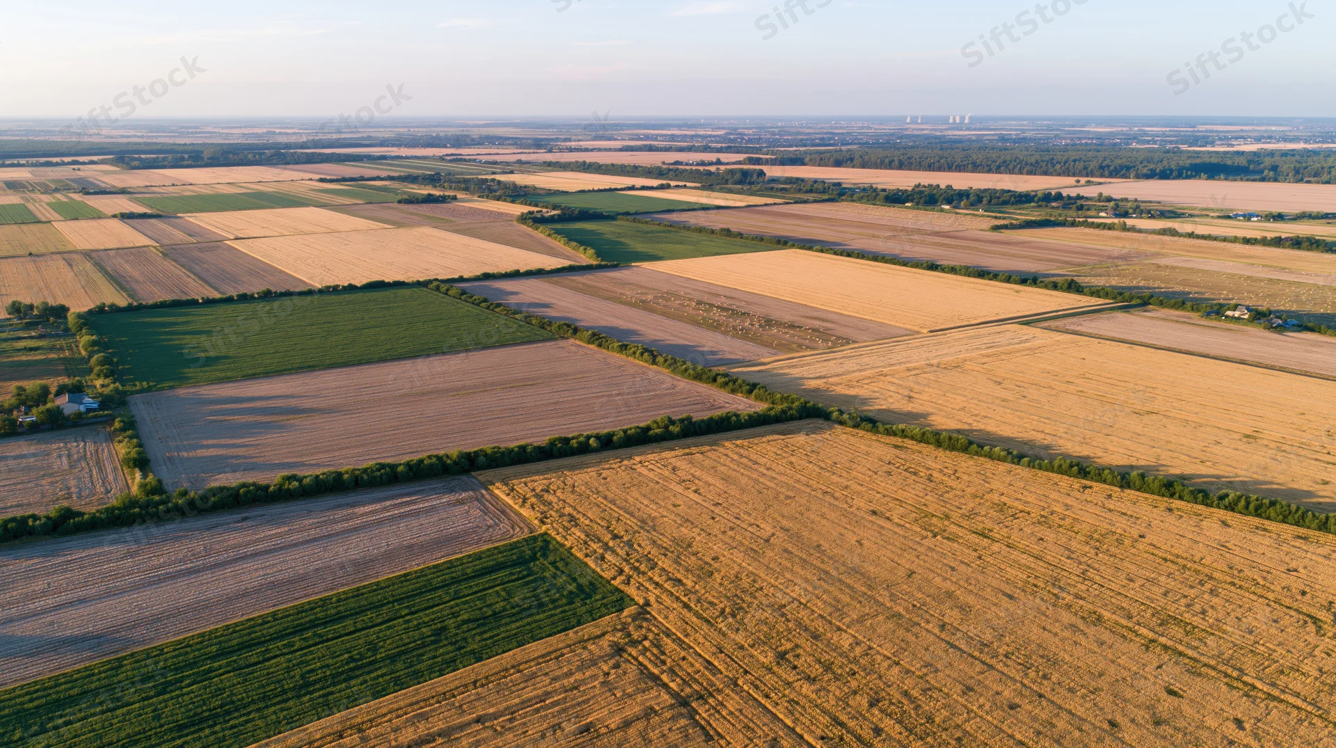 Aerial drone view of patchwork agricultural fields stretching across rural countryside under sunlight