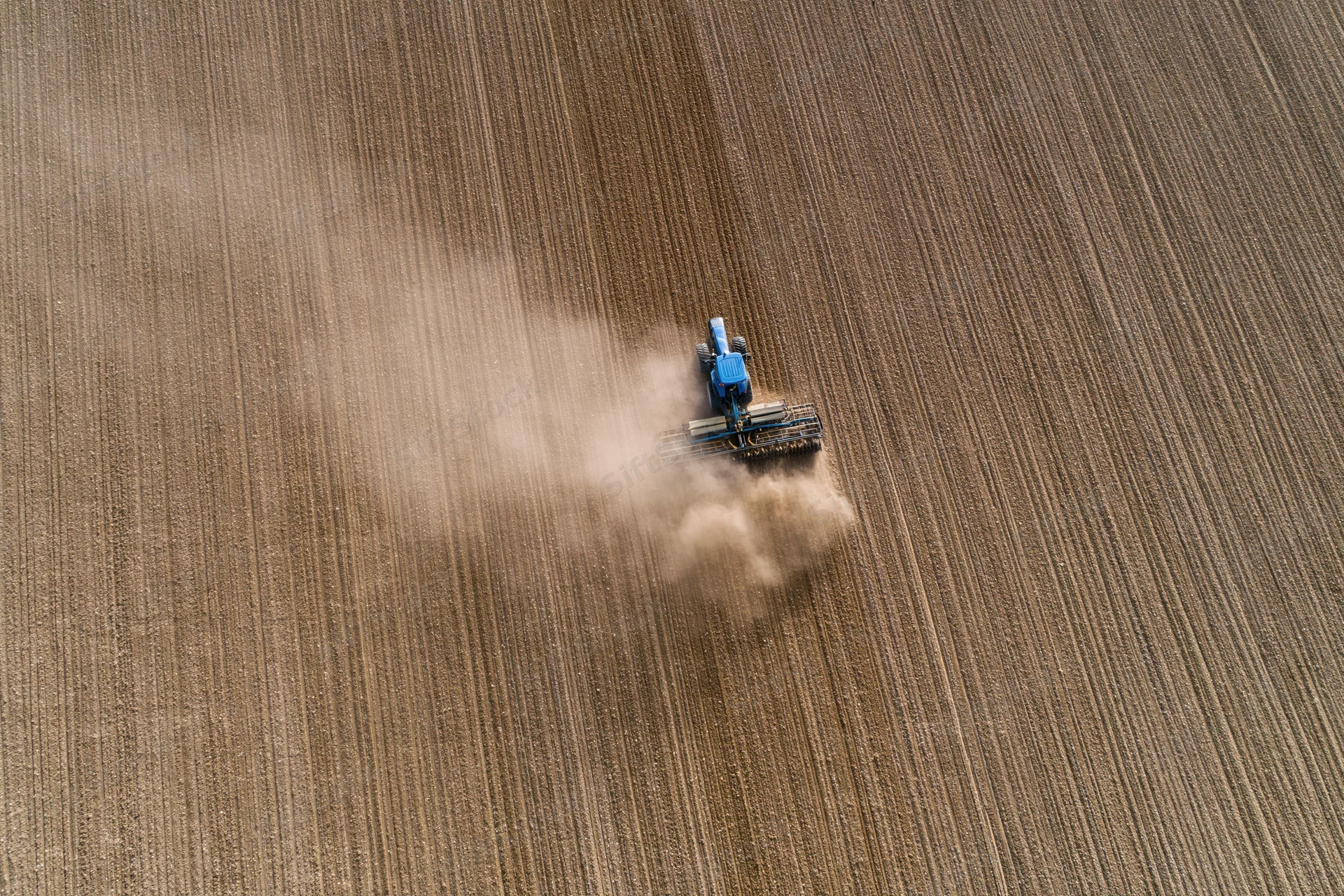Blue tractor plowing a large field from an aerial top-down view