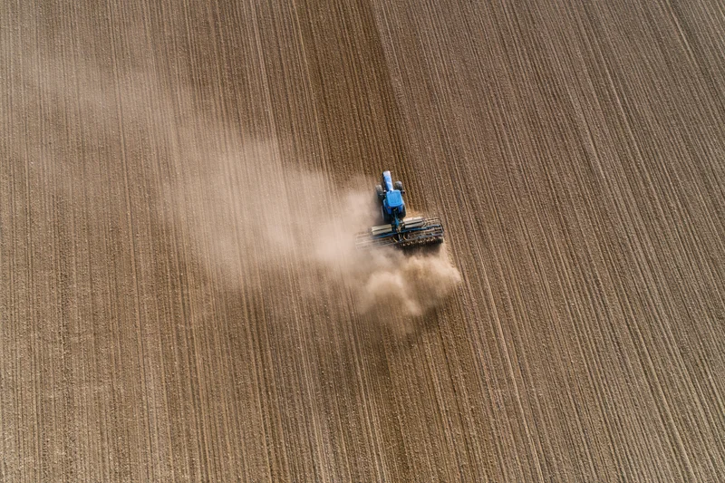 Blue tractor plowing a large field from an aerial top-down view