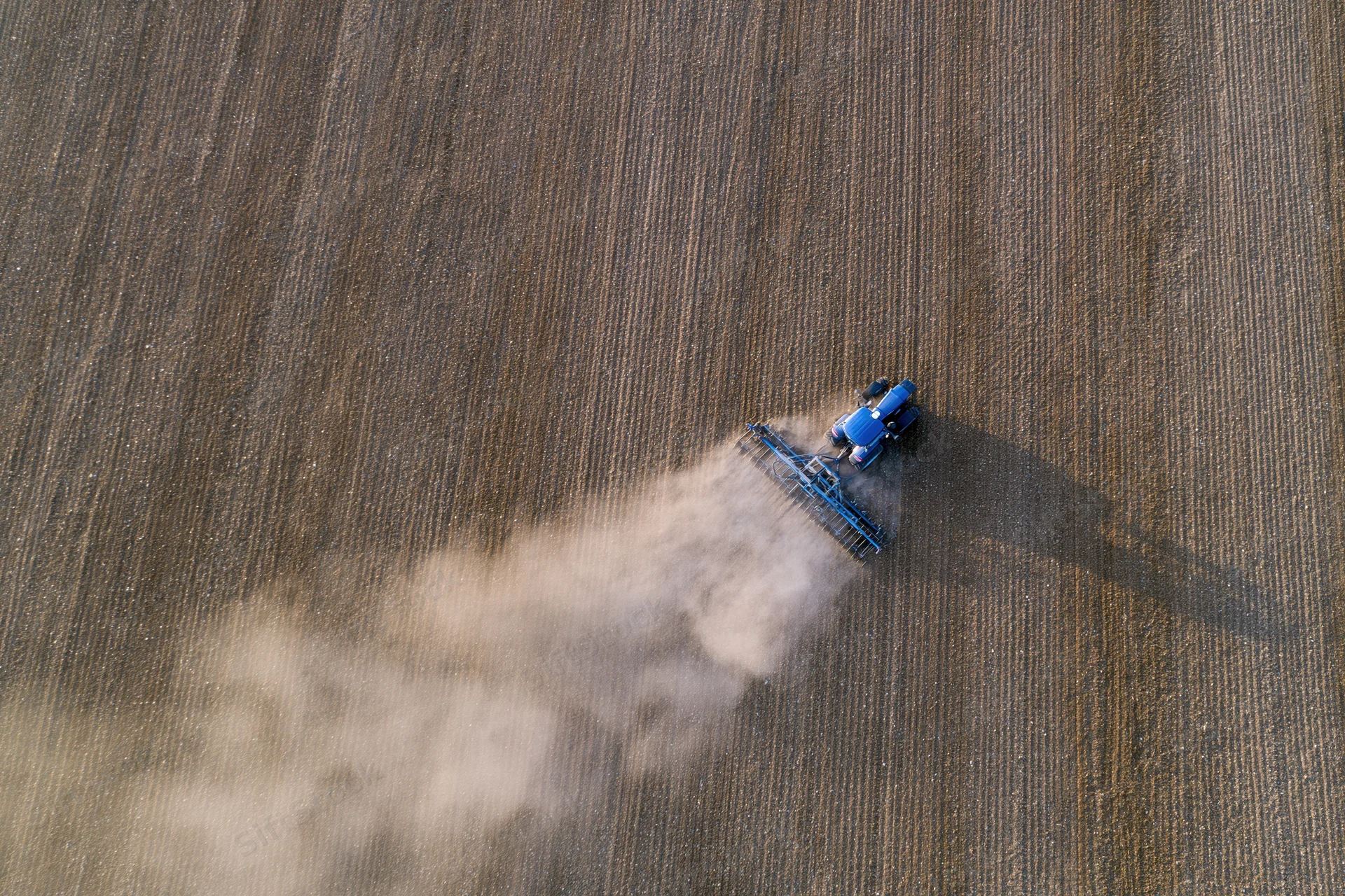 Blue tractor plowing a field from an aerial top-down view