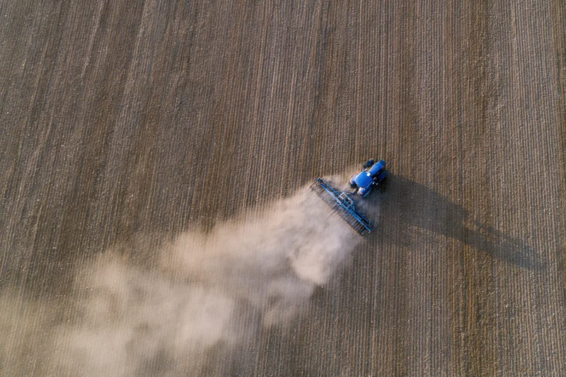 Blue tractor plowing a field from an aerial top-down view