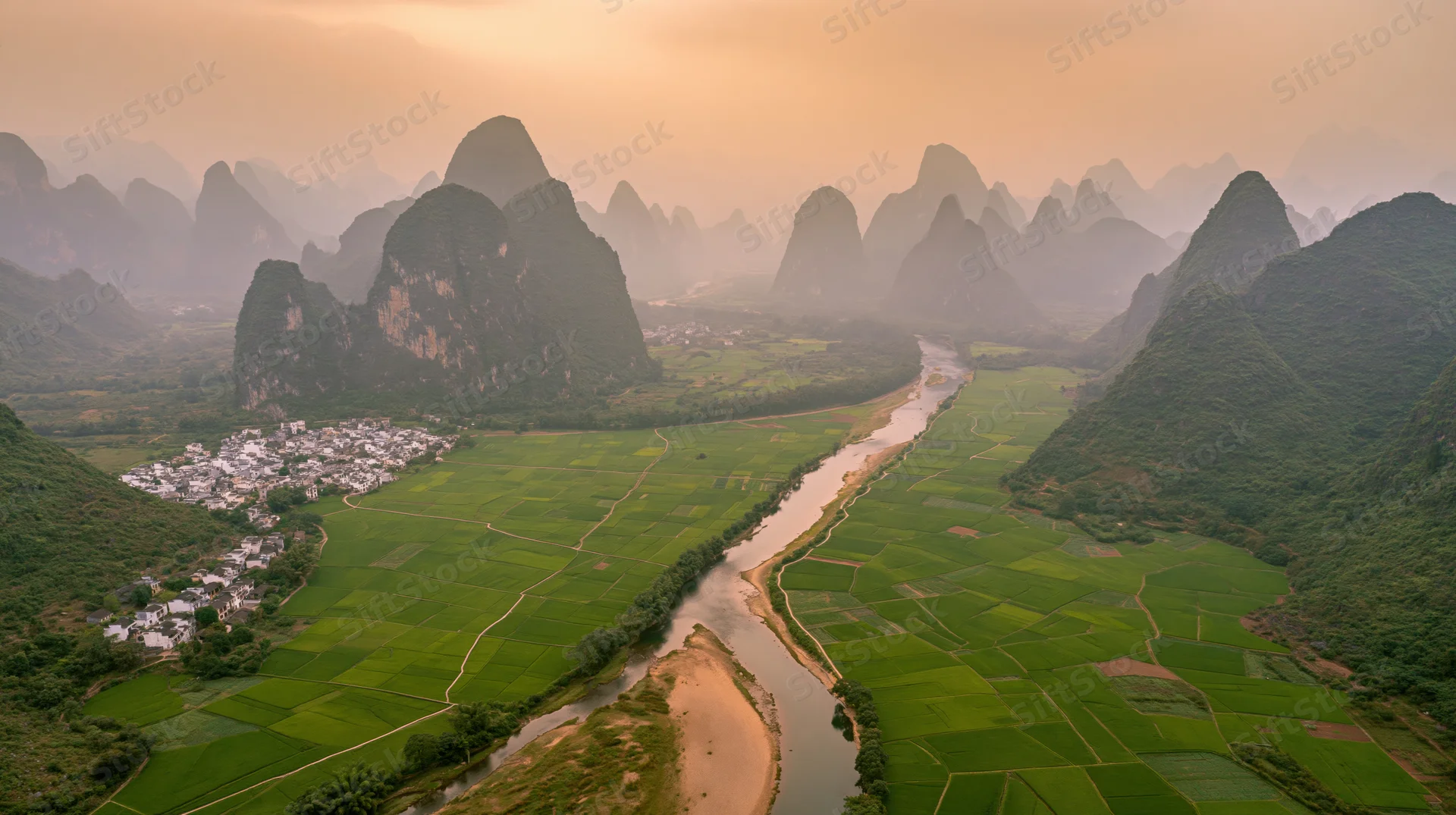 Aerial view of a river winding through green rice fields and karst mountains in a rural chinese valley