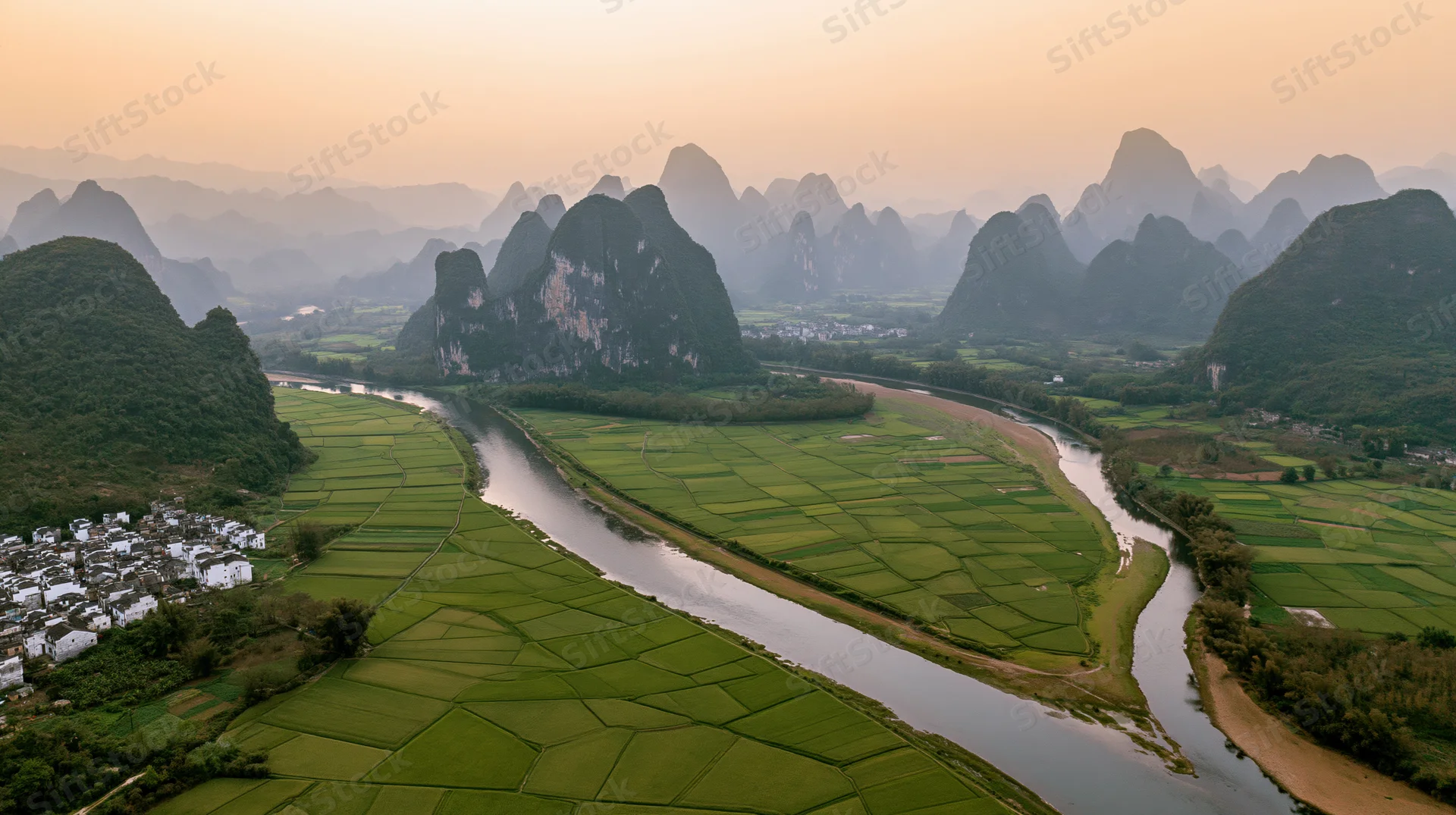 Aerial view of a winding river through green rice fields and karst mountains in a rural chinese valley