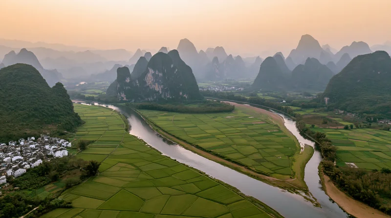 Aerial view of a winding river through green rice fields and karst mountains in a rural chinese valley