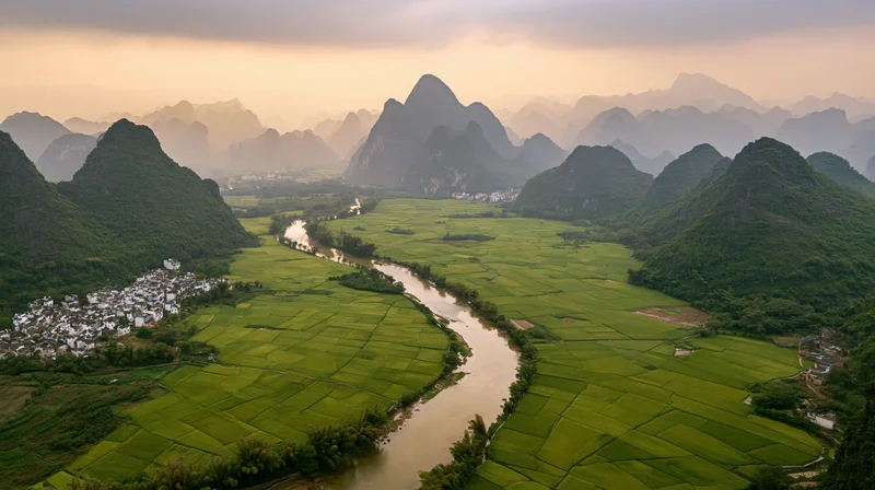 Aerial view of a winding river through green rice fields and karst mountains in a rural chinese valley