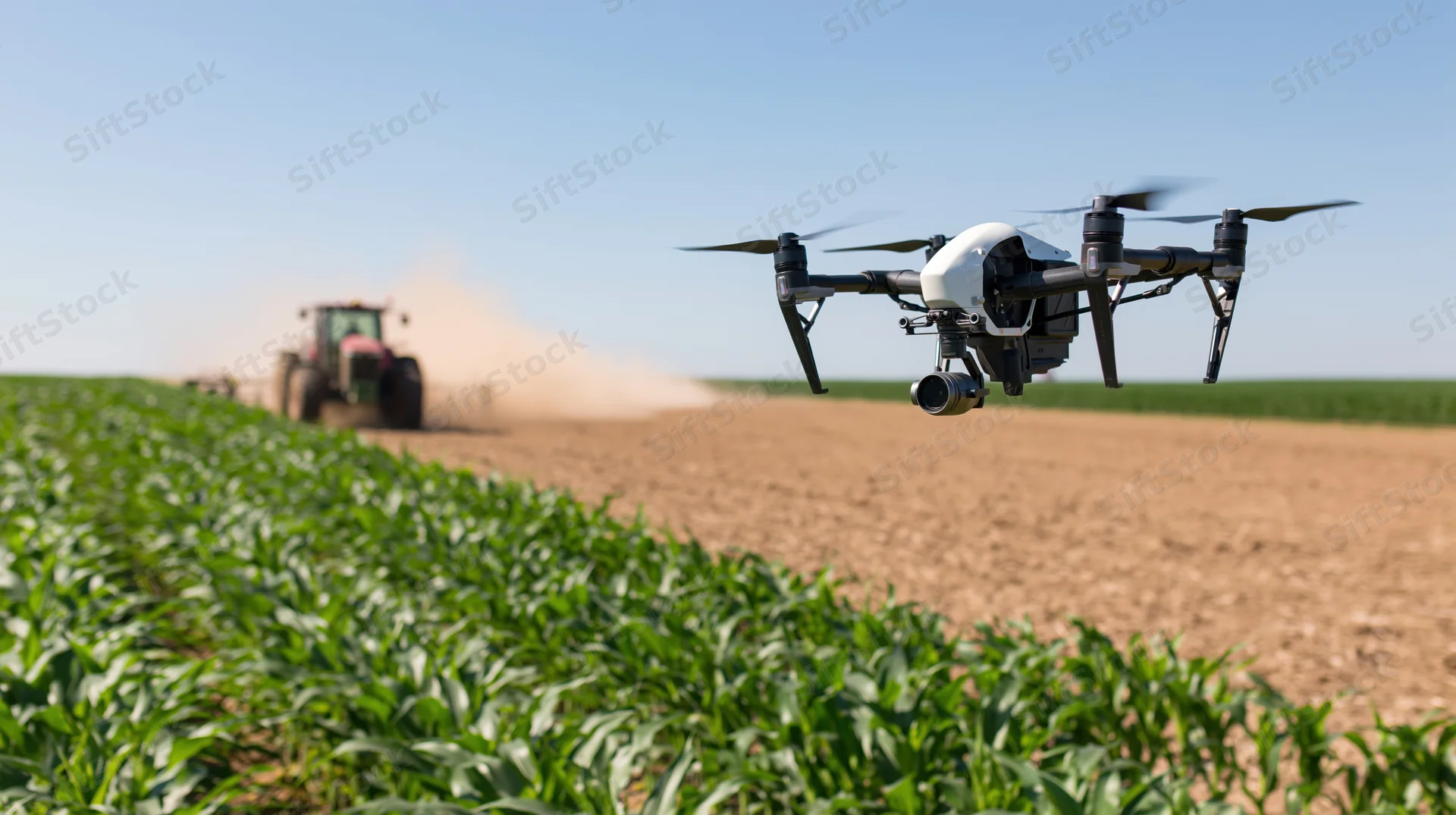 Drone hovering over cornfield with tractor tilling soil in background