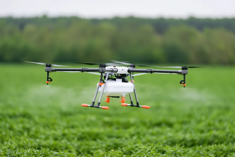 Agricultural sprayer drone hovering low over green crop field