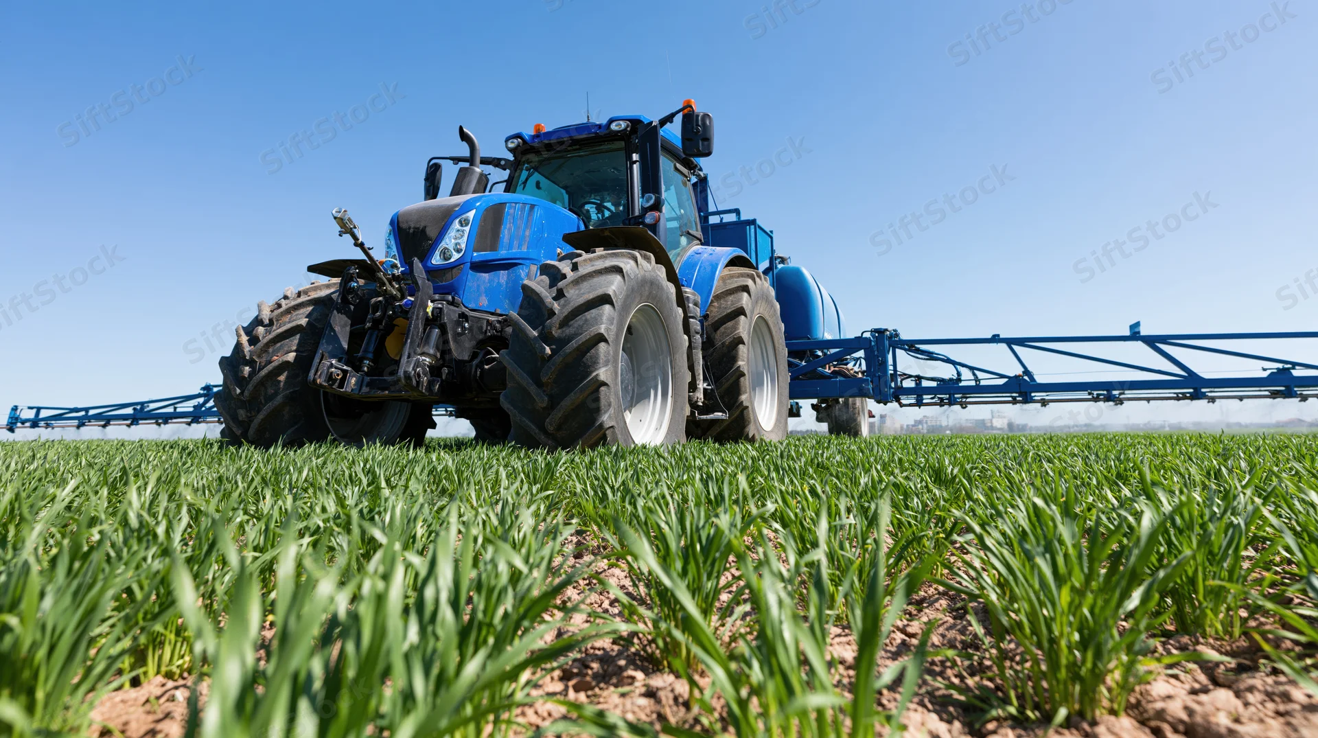 Blue tractor pulling spray boom across green crop field