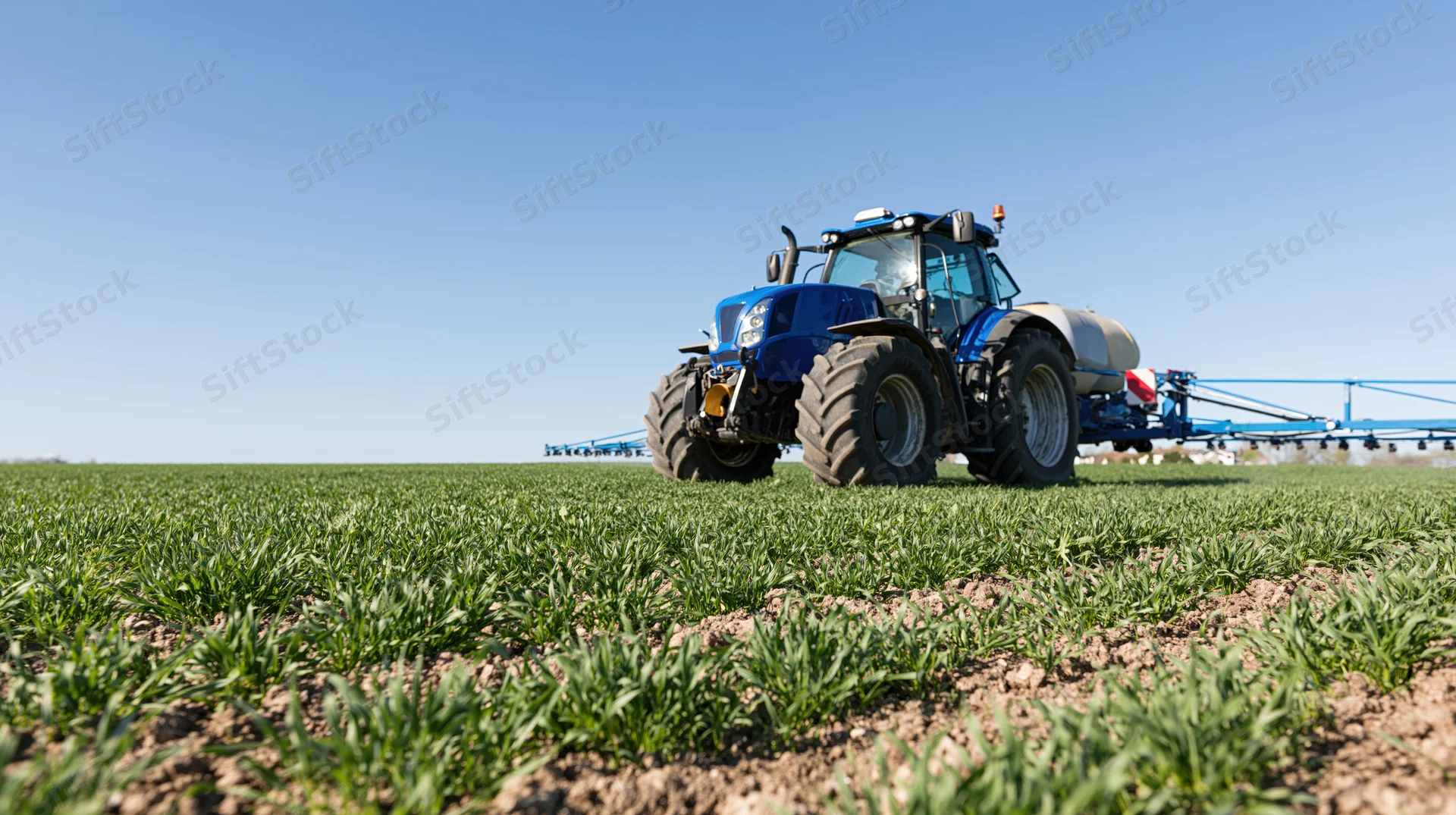 Blue tractor spraying crops in a green field under clear sky
