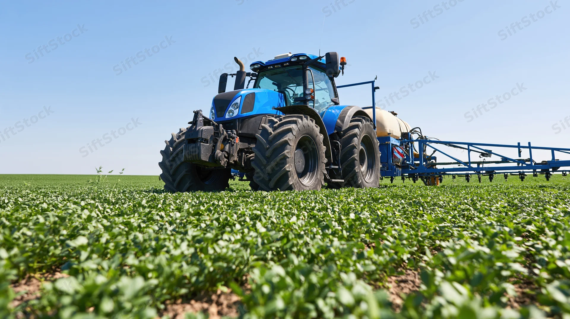 Blue tractor pulling spray boom across green soybean field