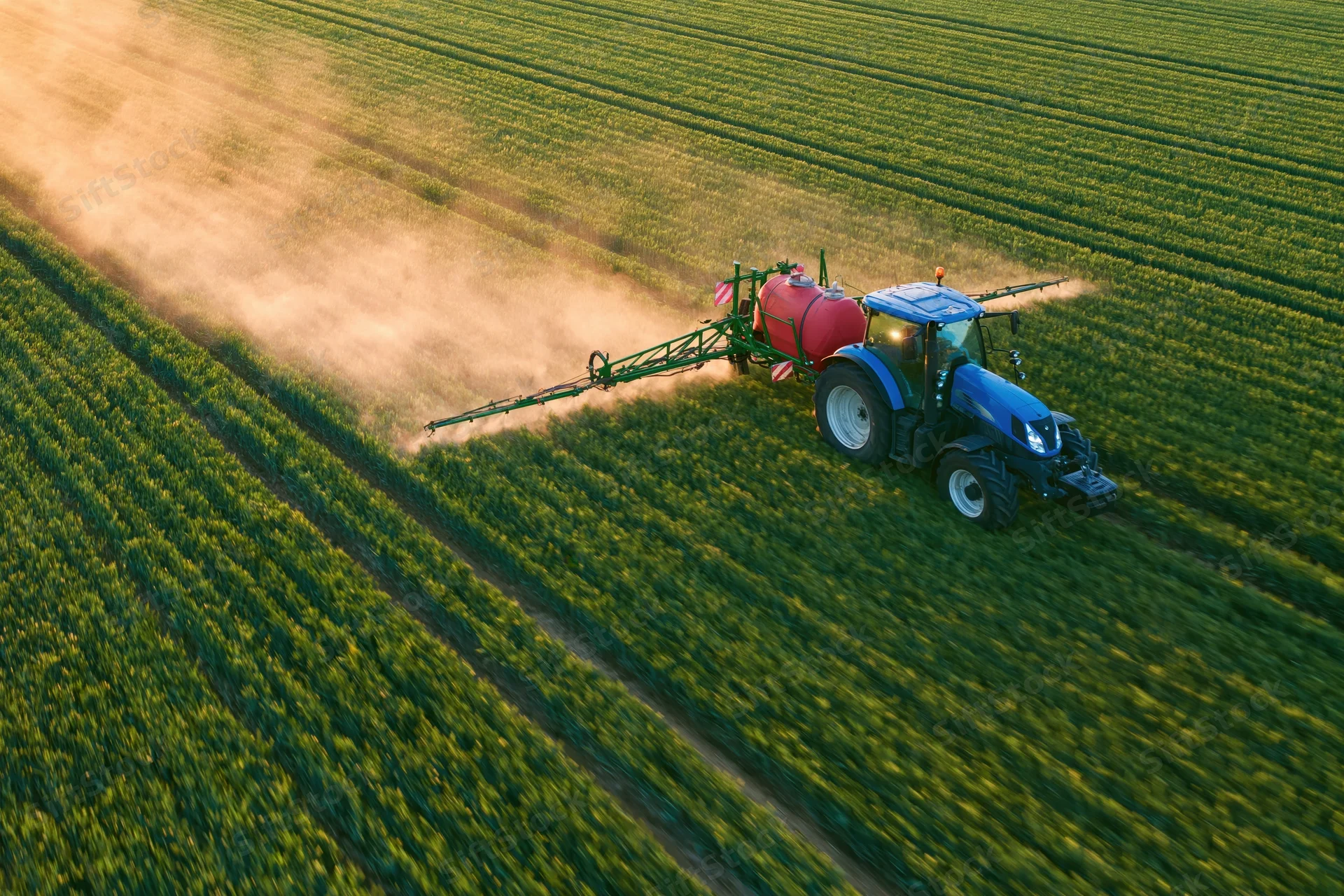Blue tractor pulling a red crop sprayer across a green field