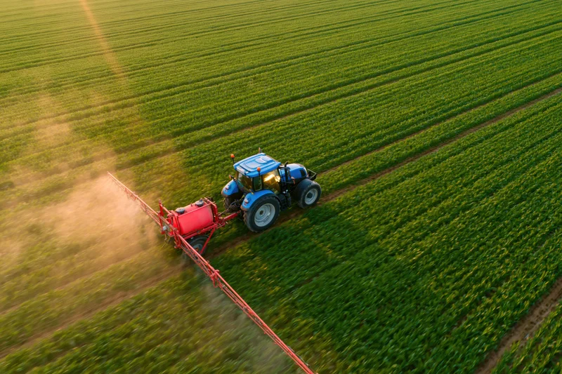 Blue tractor pulling red crop sprayer across green field
