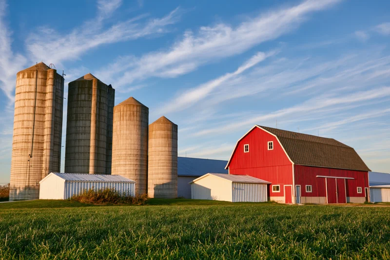 Red barn and silos on a grassy farm field under a blue sky with wispy clouds at sunset