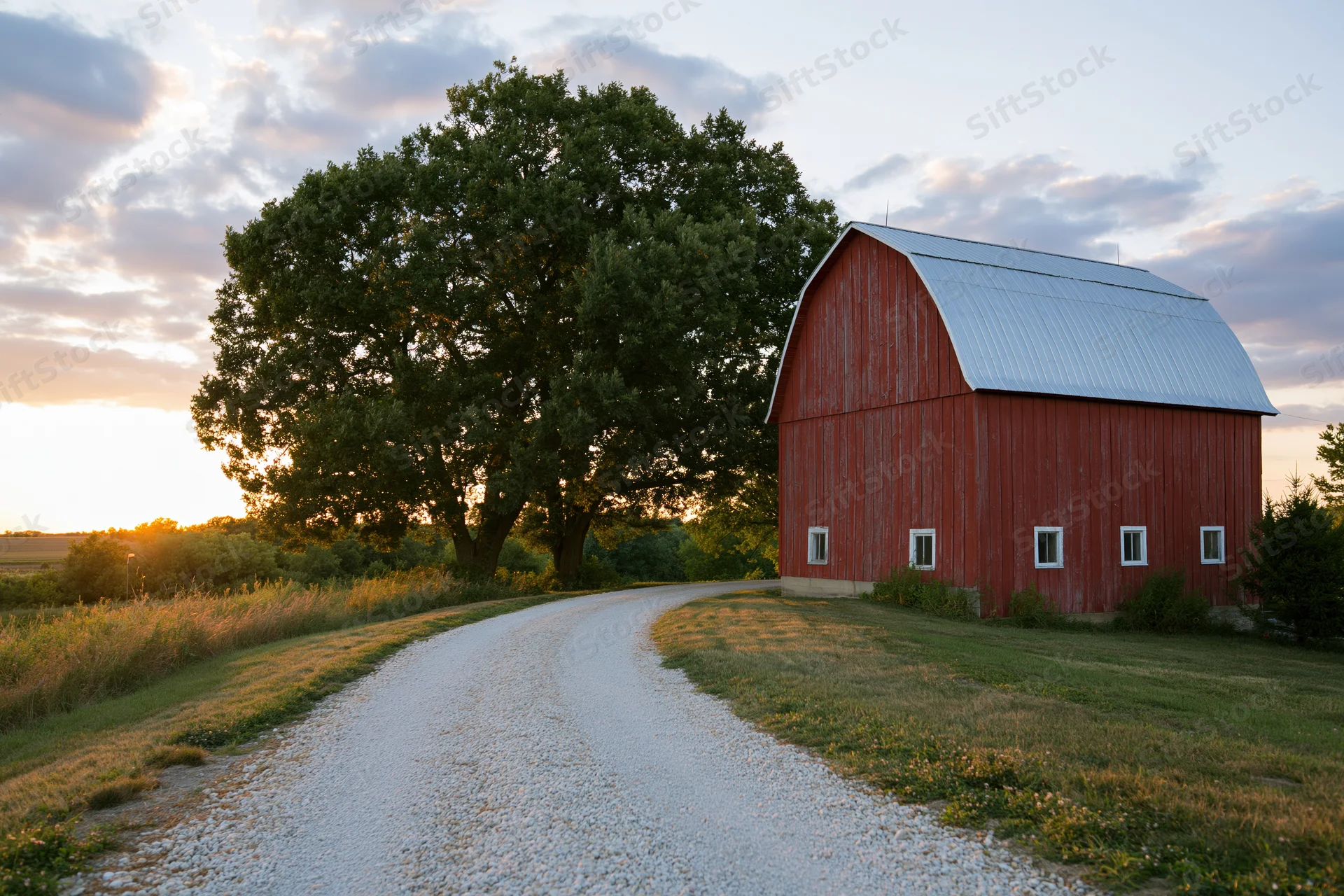 Red gambrel-roofed barn beside a gravel road on a midwestern farm at sunset
