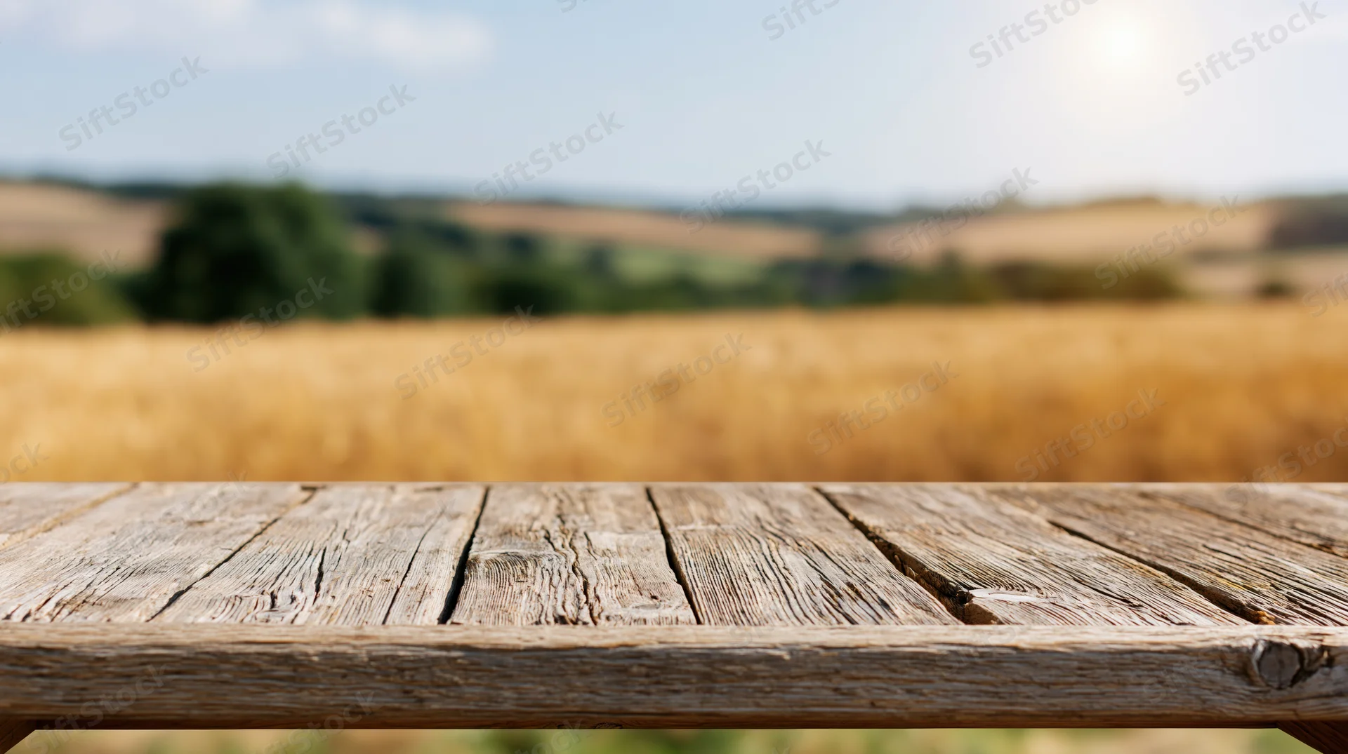 Weathered wooden table surface in front of a golden wheat field under a sunny sky