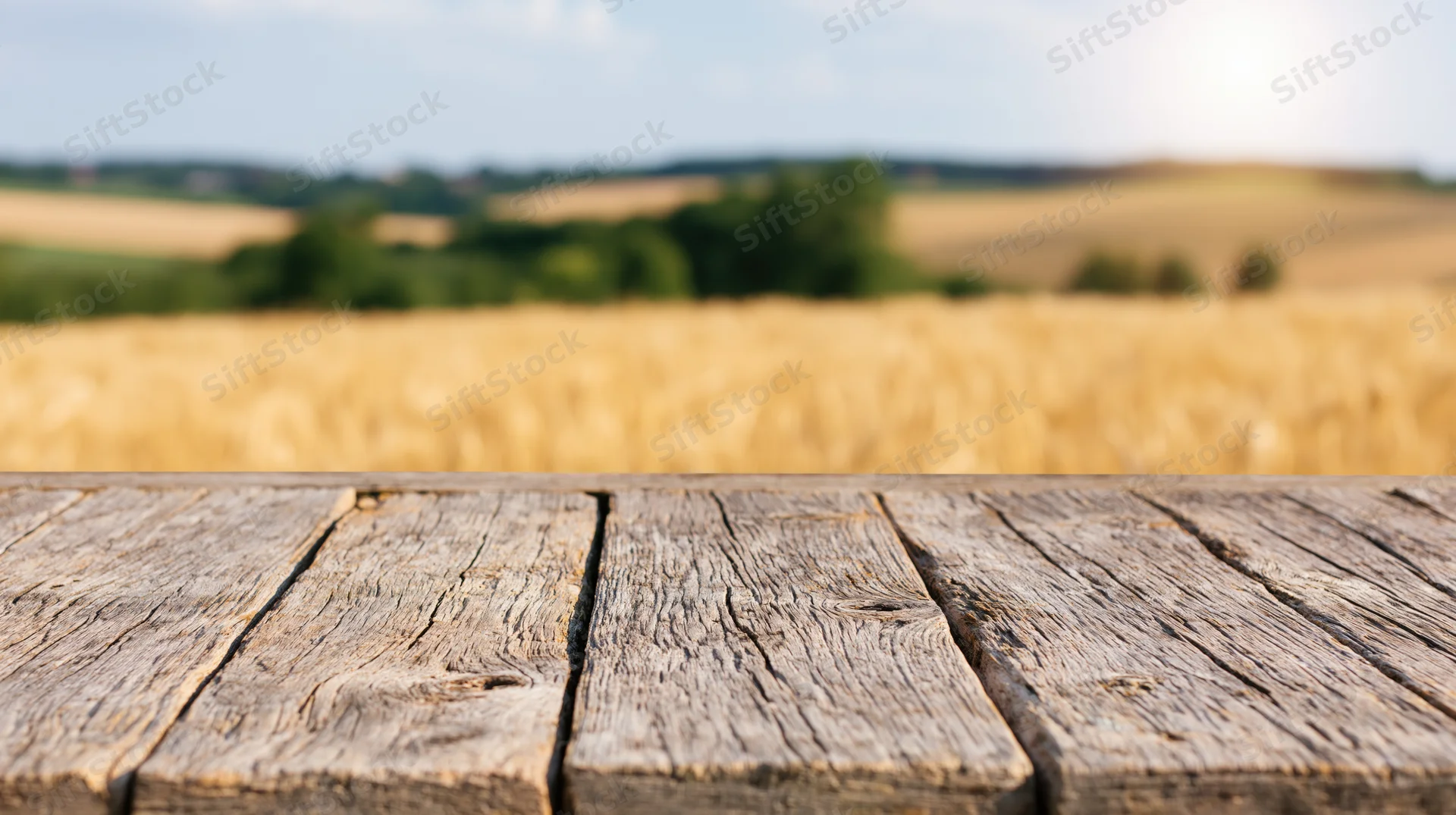 Weathered wooden plank table in foreground with blurred golden wheat field and green trees in background
