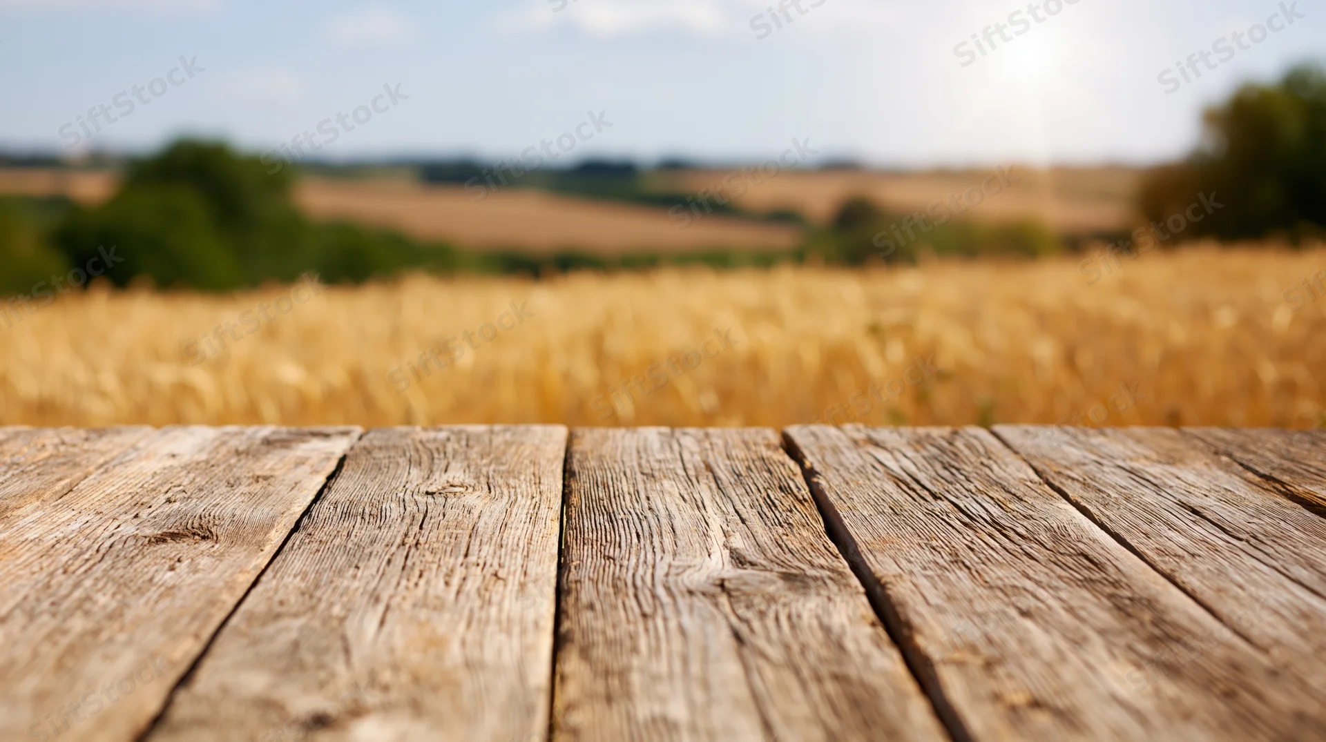Weathered wooden plank table surface in front of a golden wheat field under a sunny sky