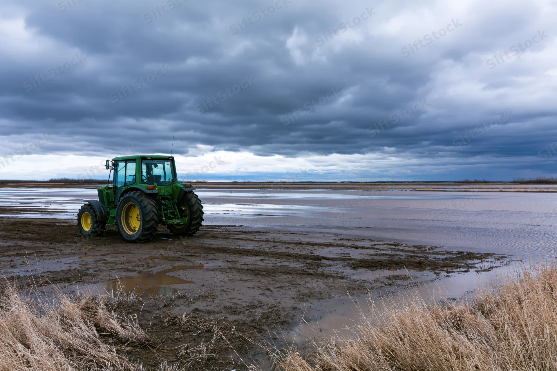 Green john deere tractor parked on muddy waterlogged field under cloudy sky