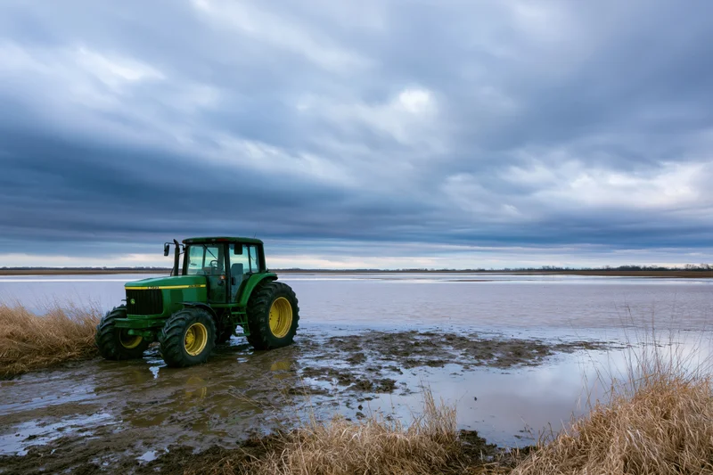 Green john deere tractor parked on muddy waterlogged field under cloudy sky