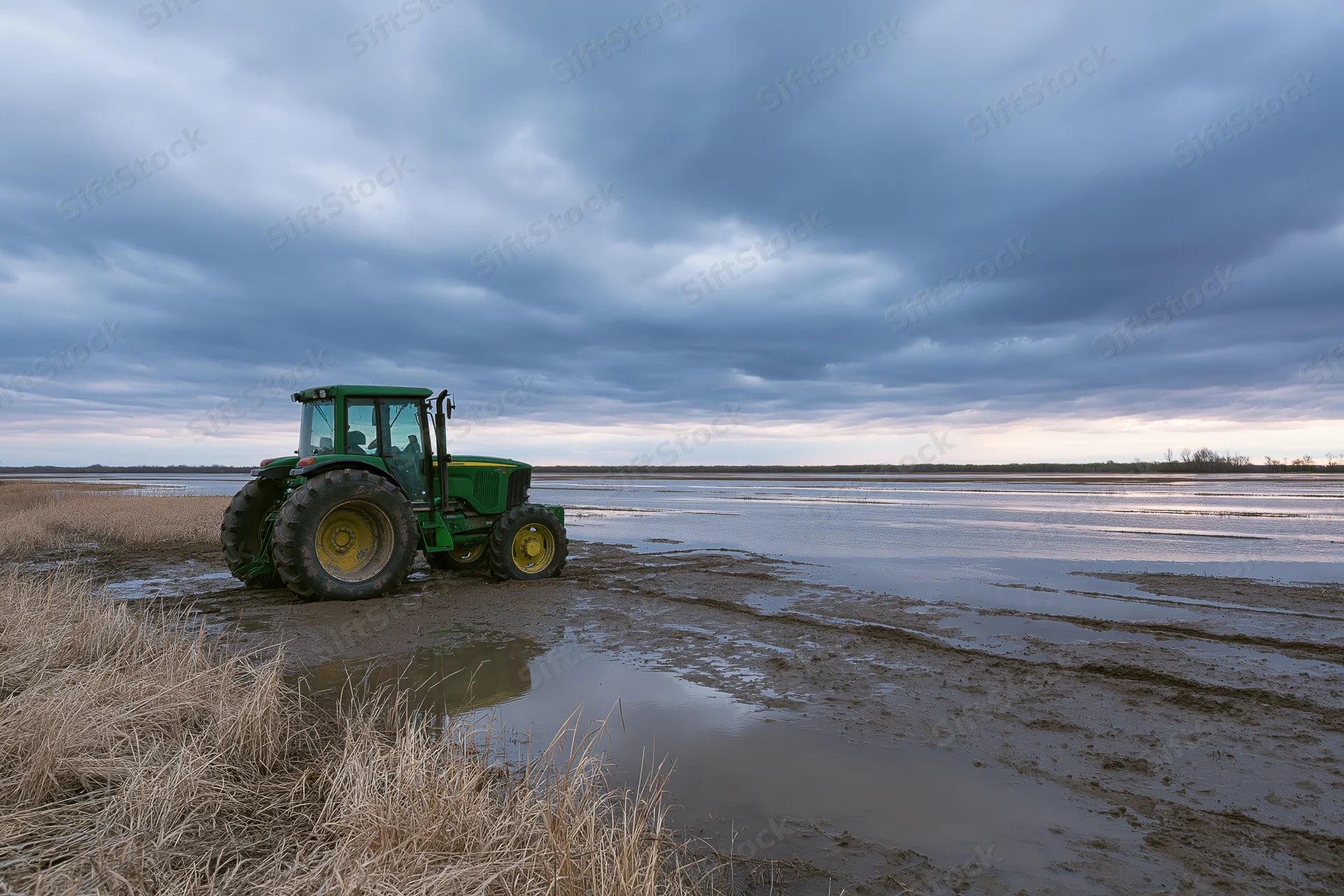 Green john deere tractor parked on muddy waterlogged field under cloudy sky