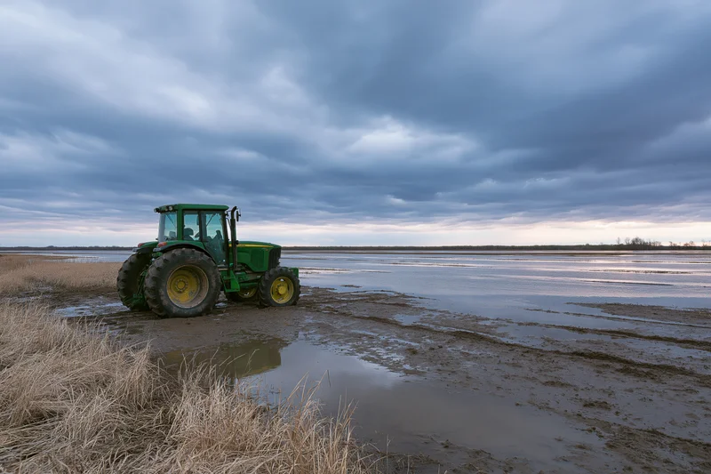 Green john deere tractor parked on muddy waterlogged field under cloudy sky
