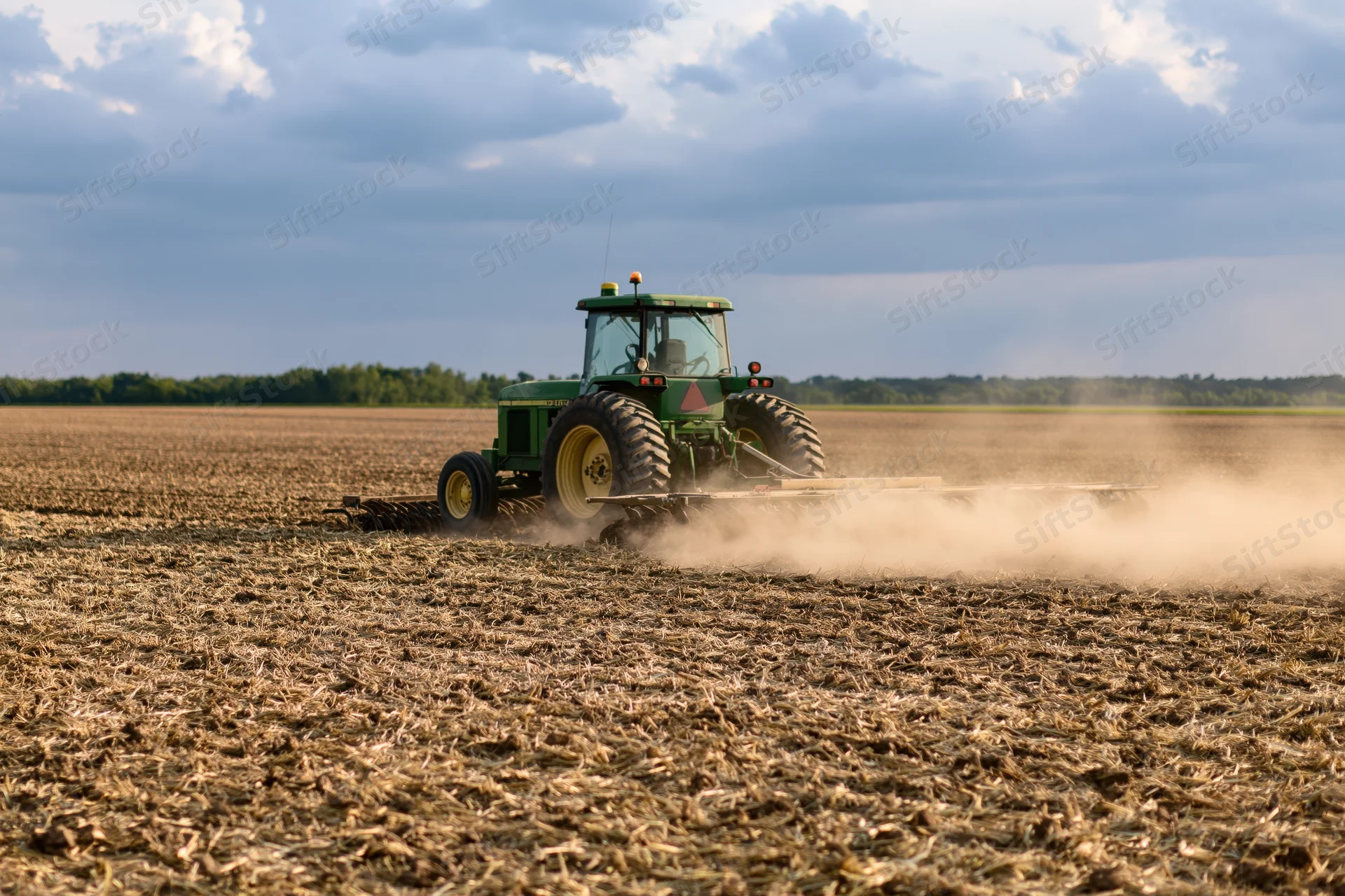 Green tractor pulling disc harrow across dry harvested field
