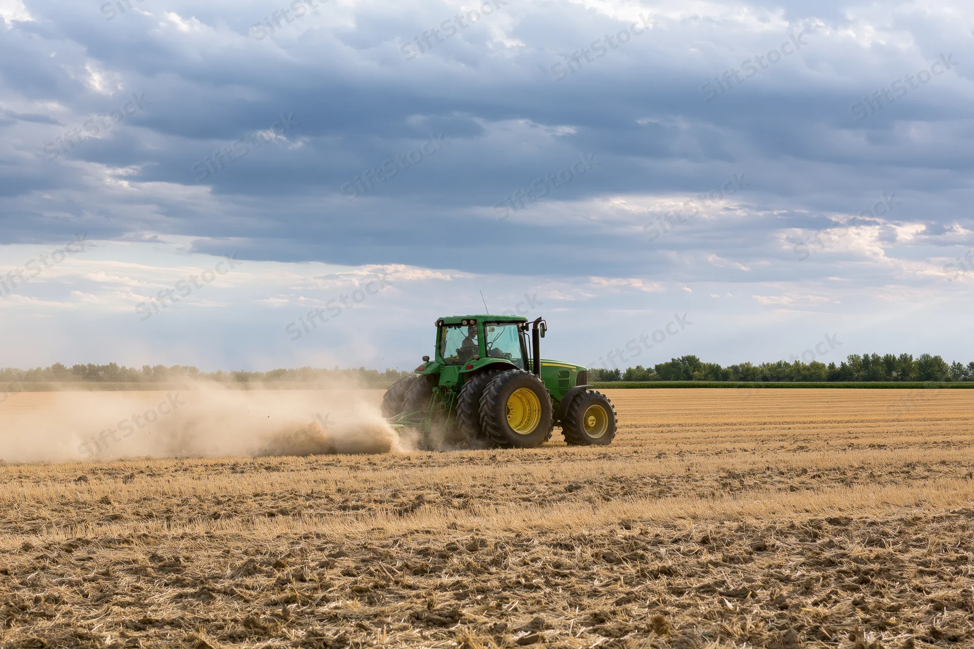 Green tractor pulling disc harrow across dry harvested field