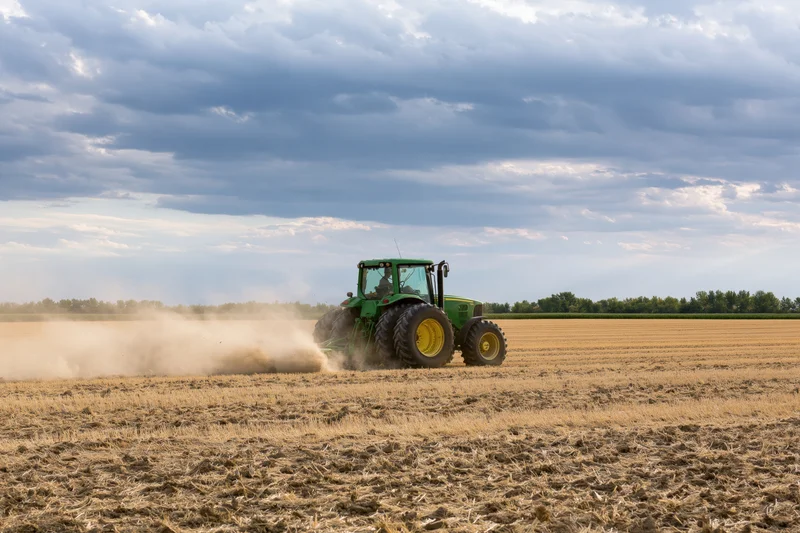 Green tractor pulling disc harrow across dry harvested field
