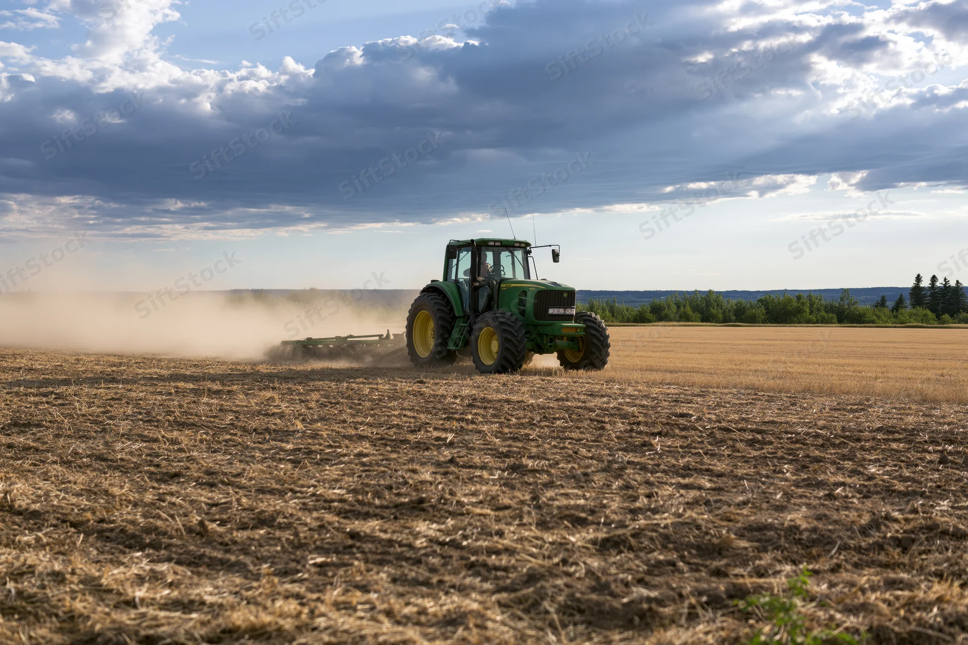 Green tractor pulling disc harrow across dry harvested field