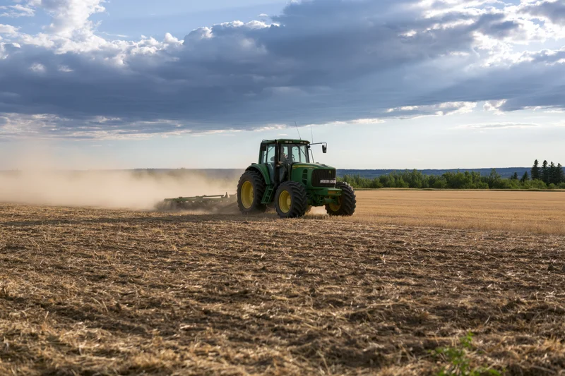 Green tractor pulling disc harrow across dry harvested field