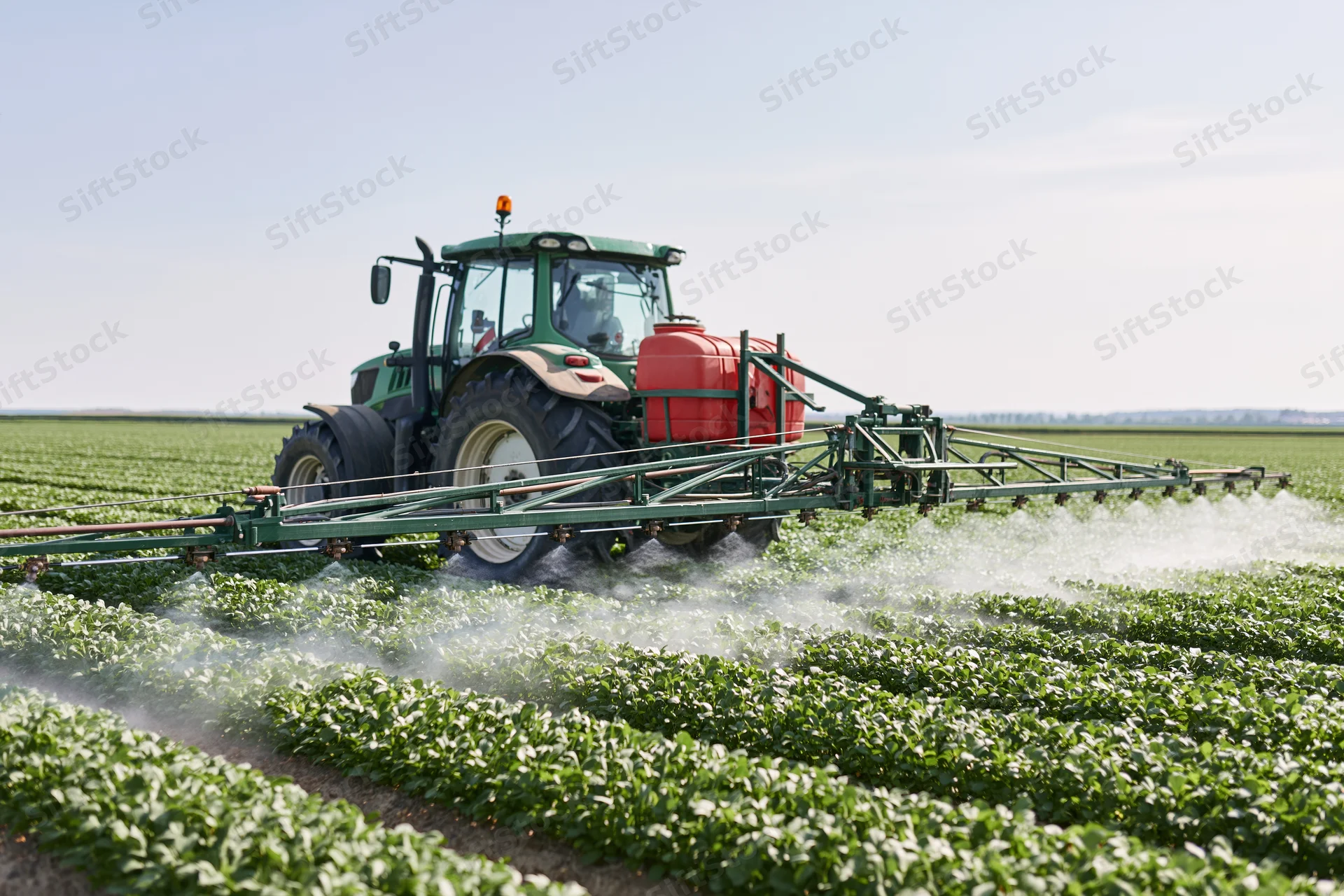 Green tractor pulling boom sprayer across rows of crops in a field