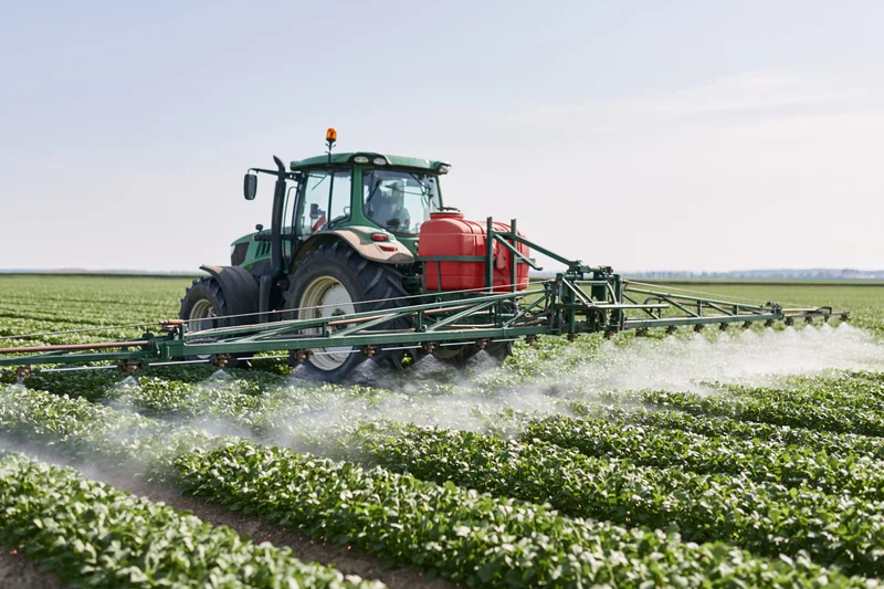 Green tractor pulling boom sprayer across rows of crops in a field