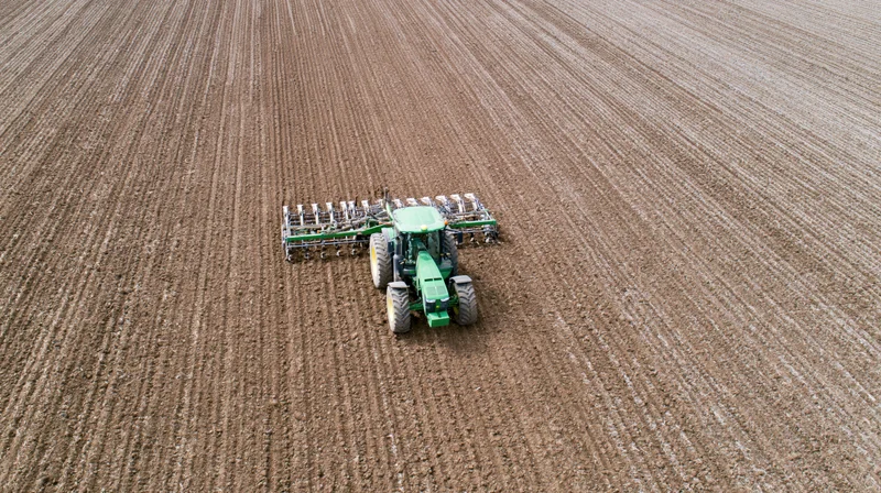 Green tractor pulling a wide cultivator across a tilled field