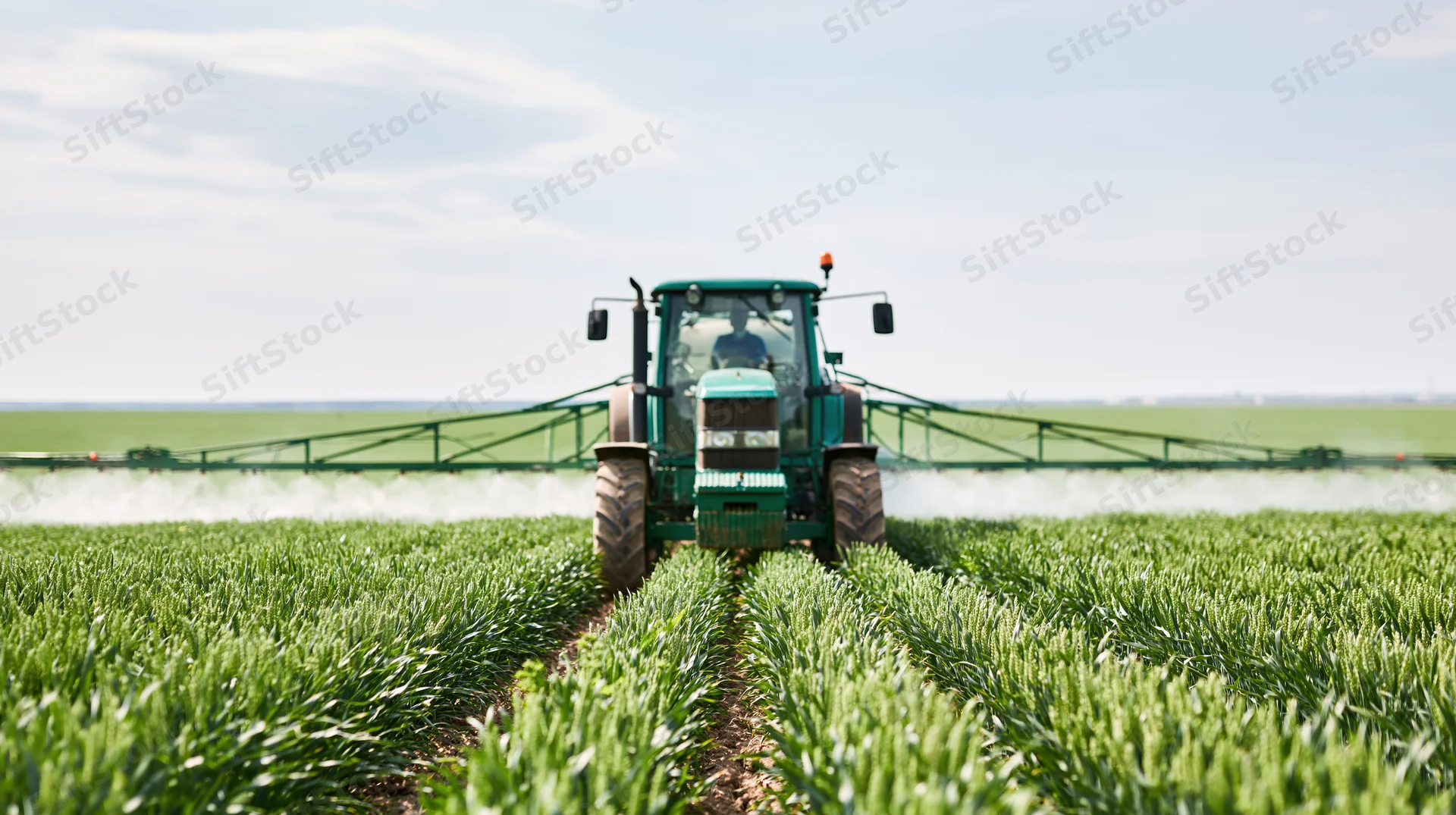 Green tractor spraying crops in a field with wide boom attachment