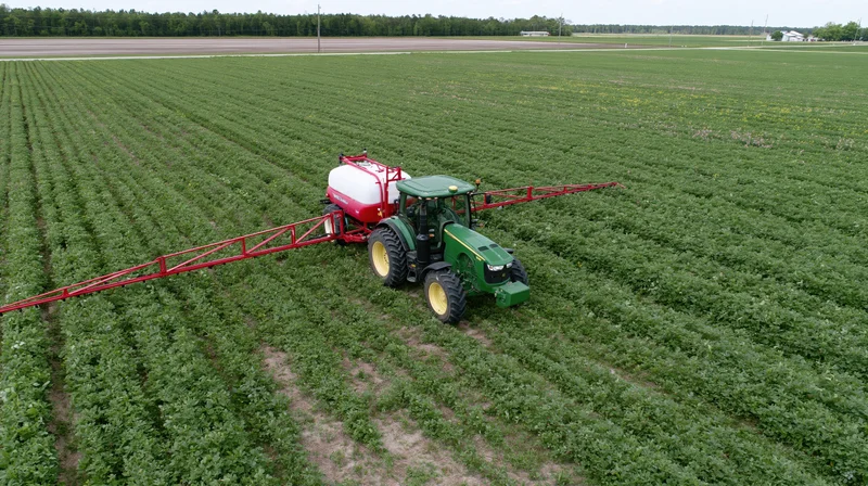Green tractor pulling a red boom sprayer across farmland