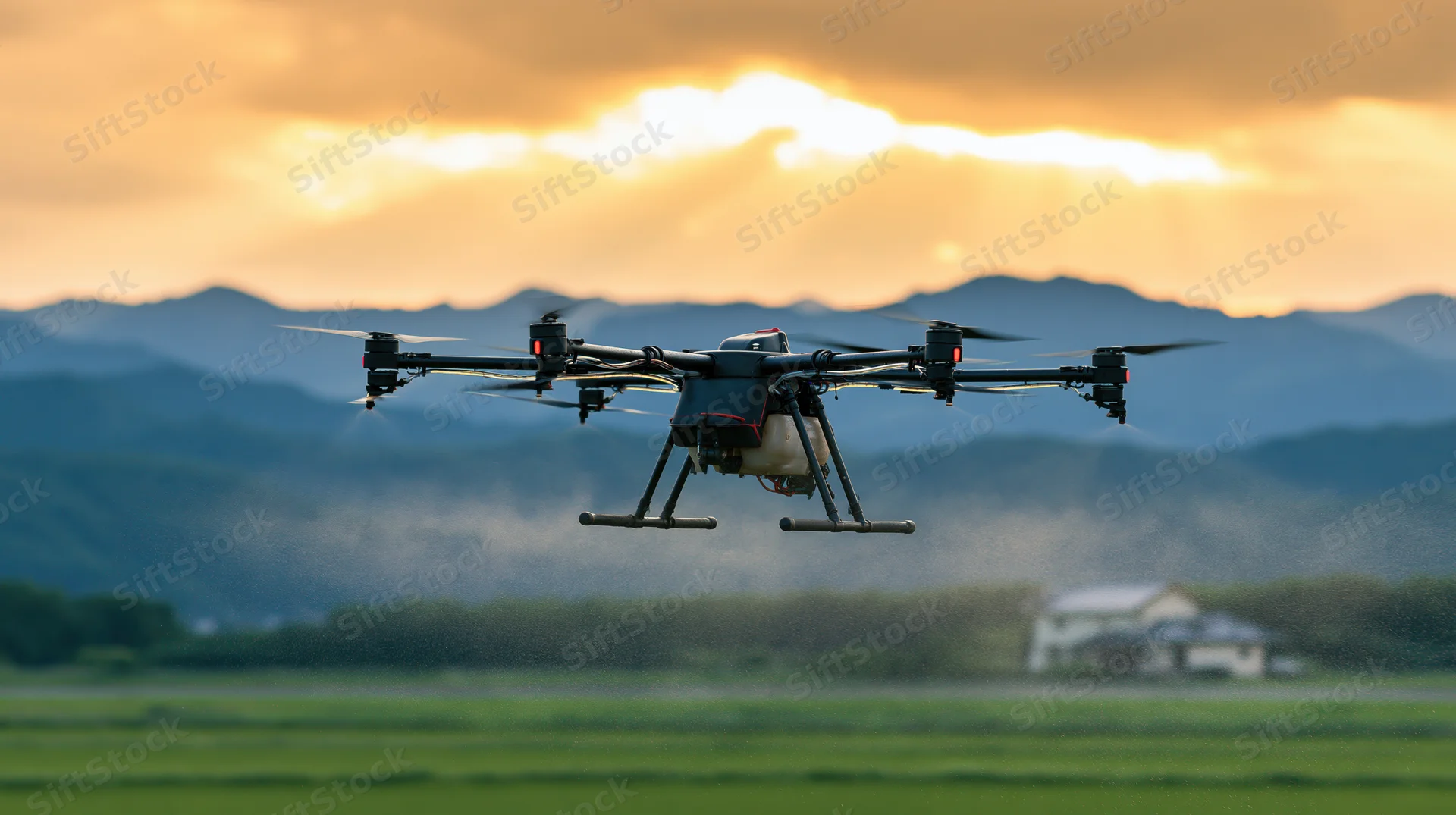 Agricultural sprayer drone hovering low over green field at sunset with mountains in background