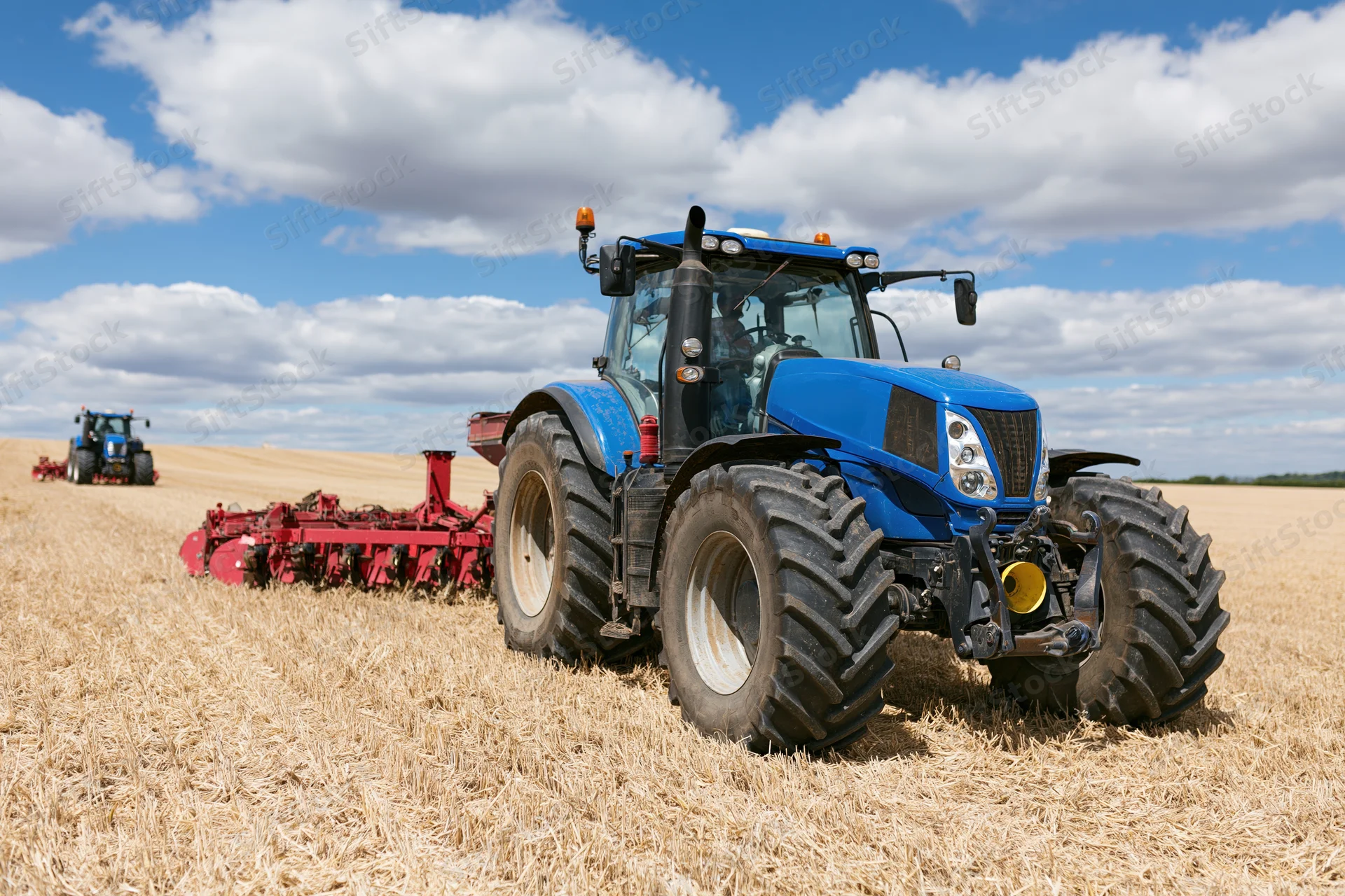 Blue tractor pulling red disc harrow in harvested field