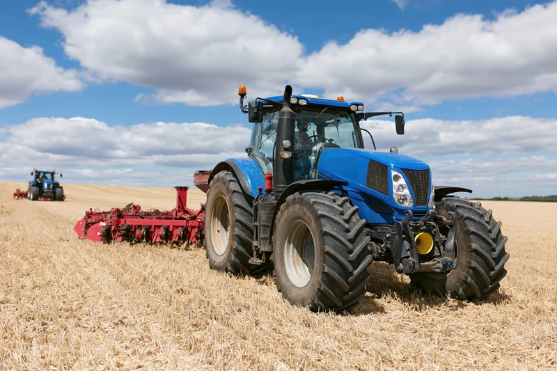 Blue tractor pulling red disc harrow in harvested field