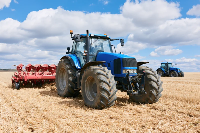 Blue tractor pulling red disc harrow in harvested field