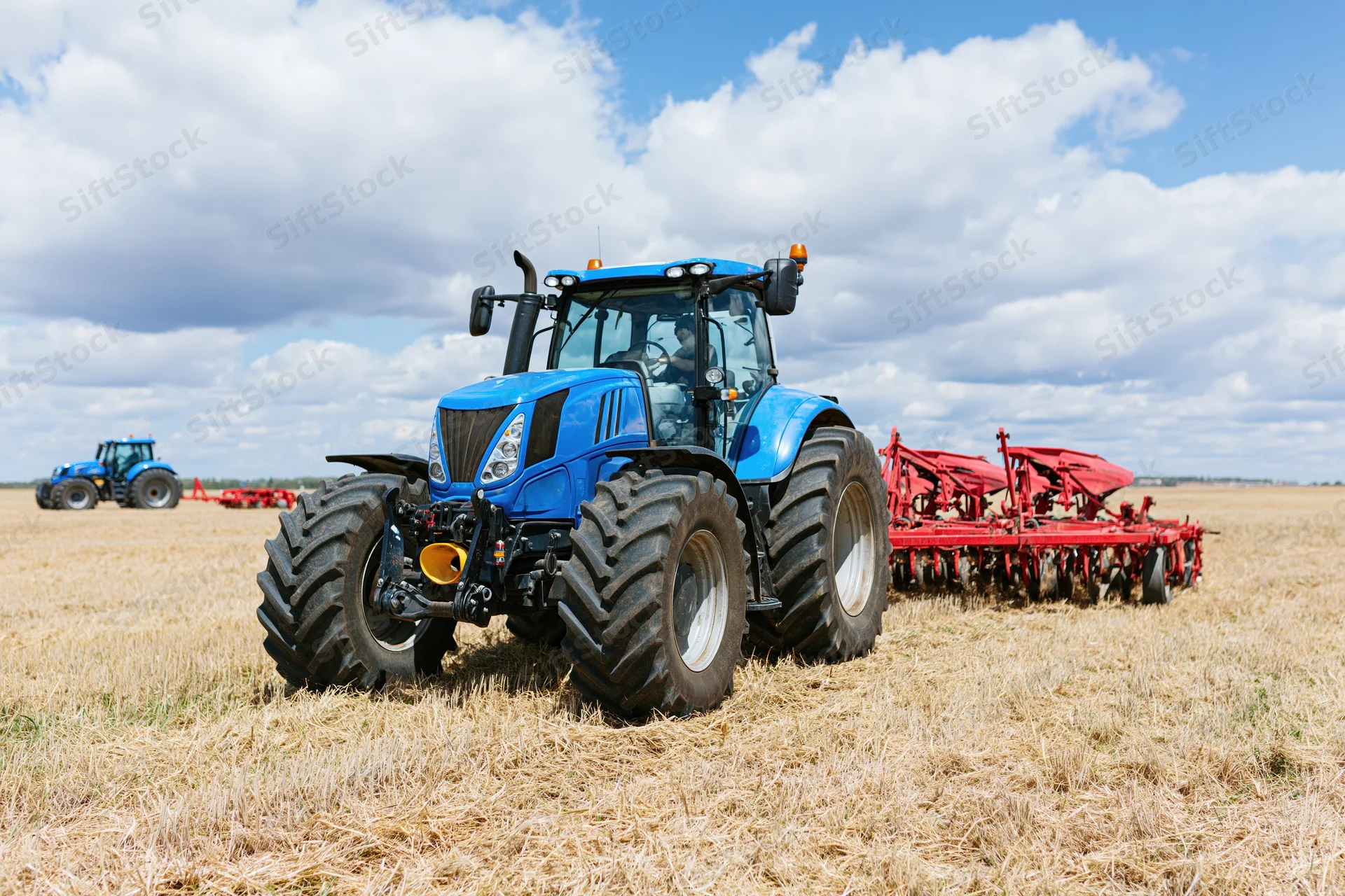 Large blue farm tractor pulling a red disc harrow attachment