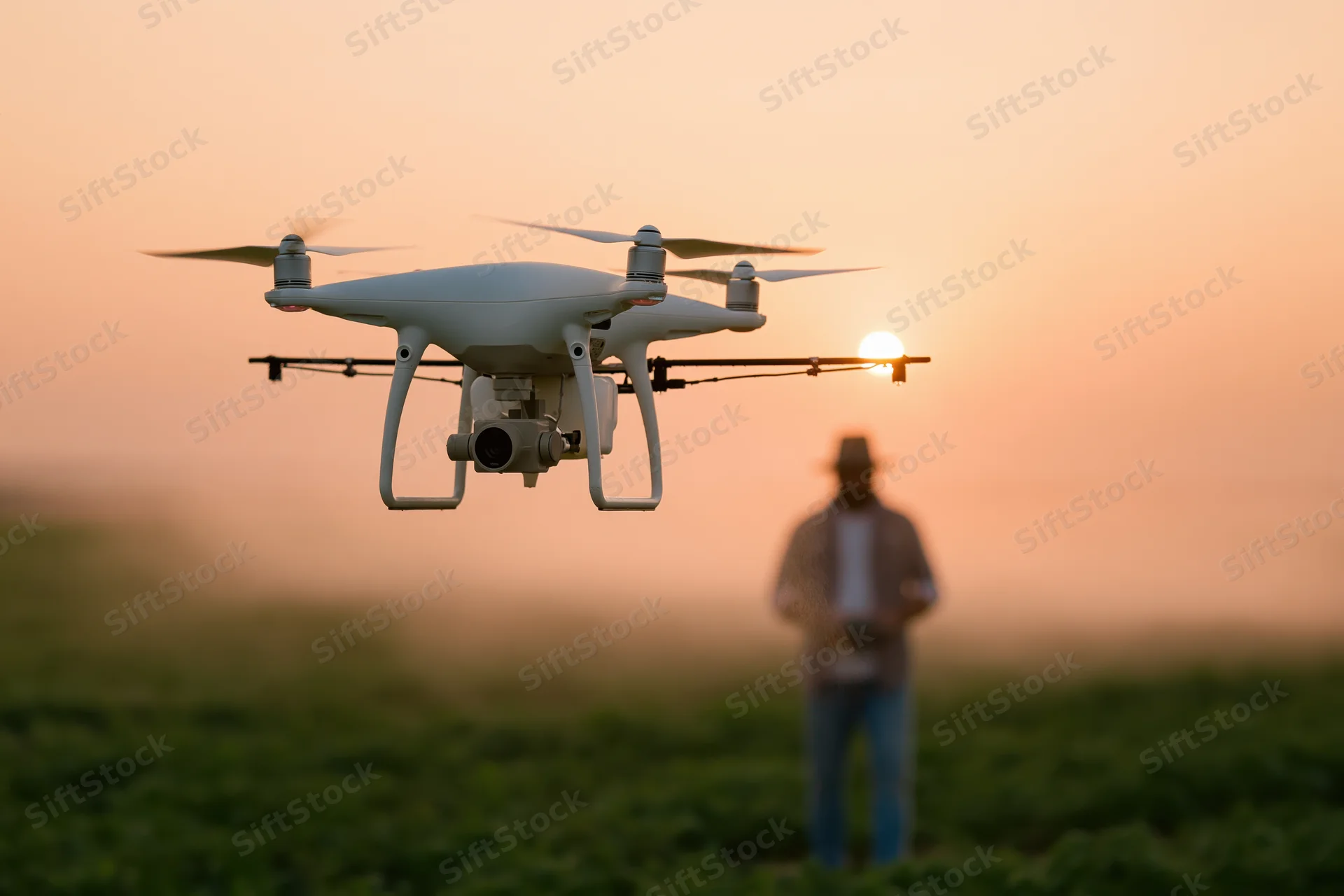 White drone hovering over green field at sunset with farmer in background